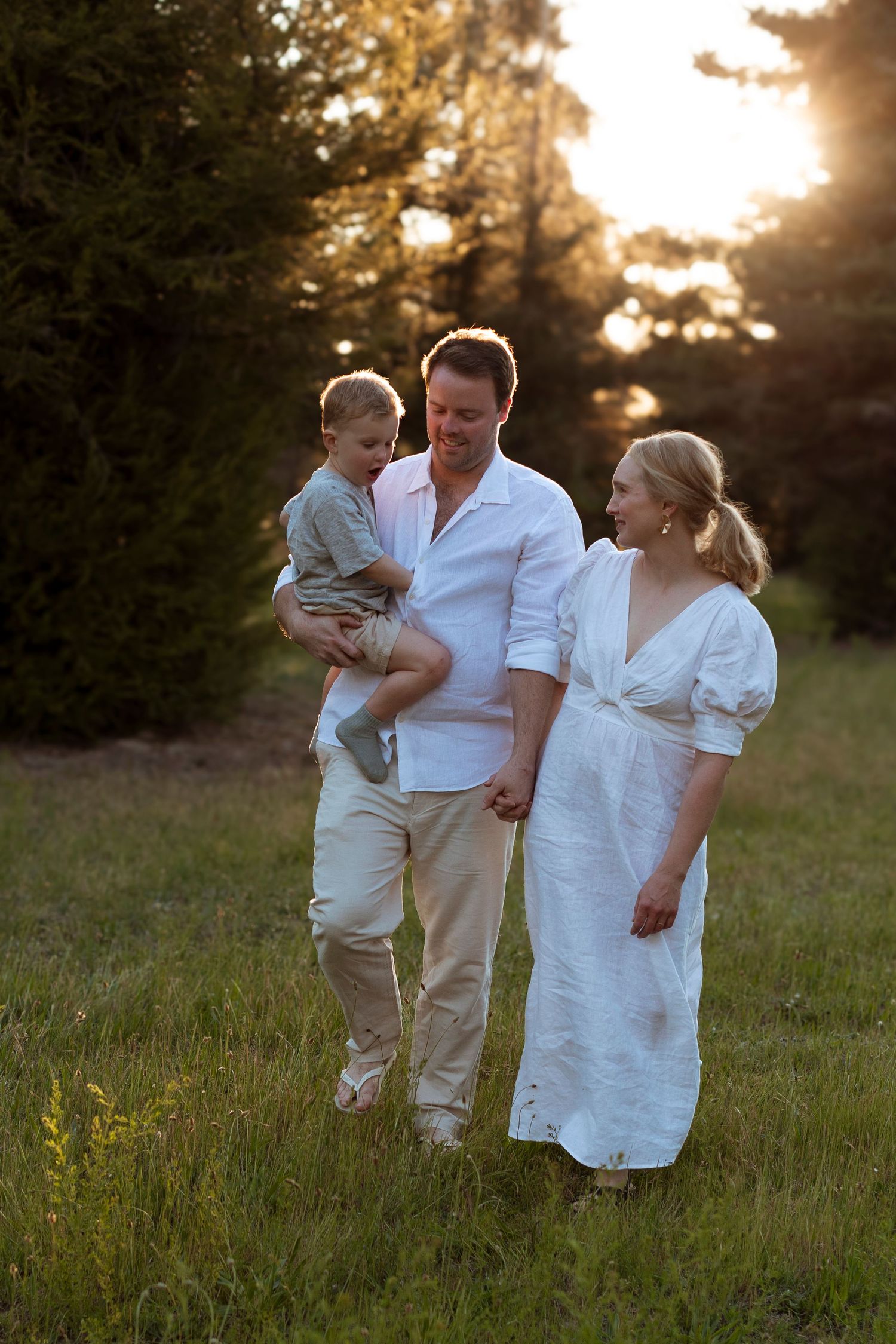 Family in white outfits enjoying tender moments together in grassy field at golden hour.