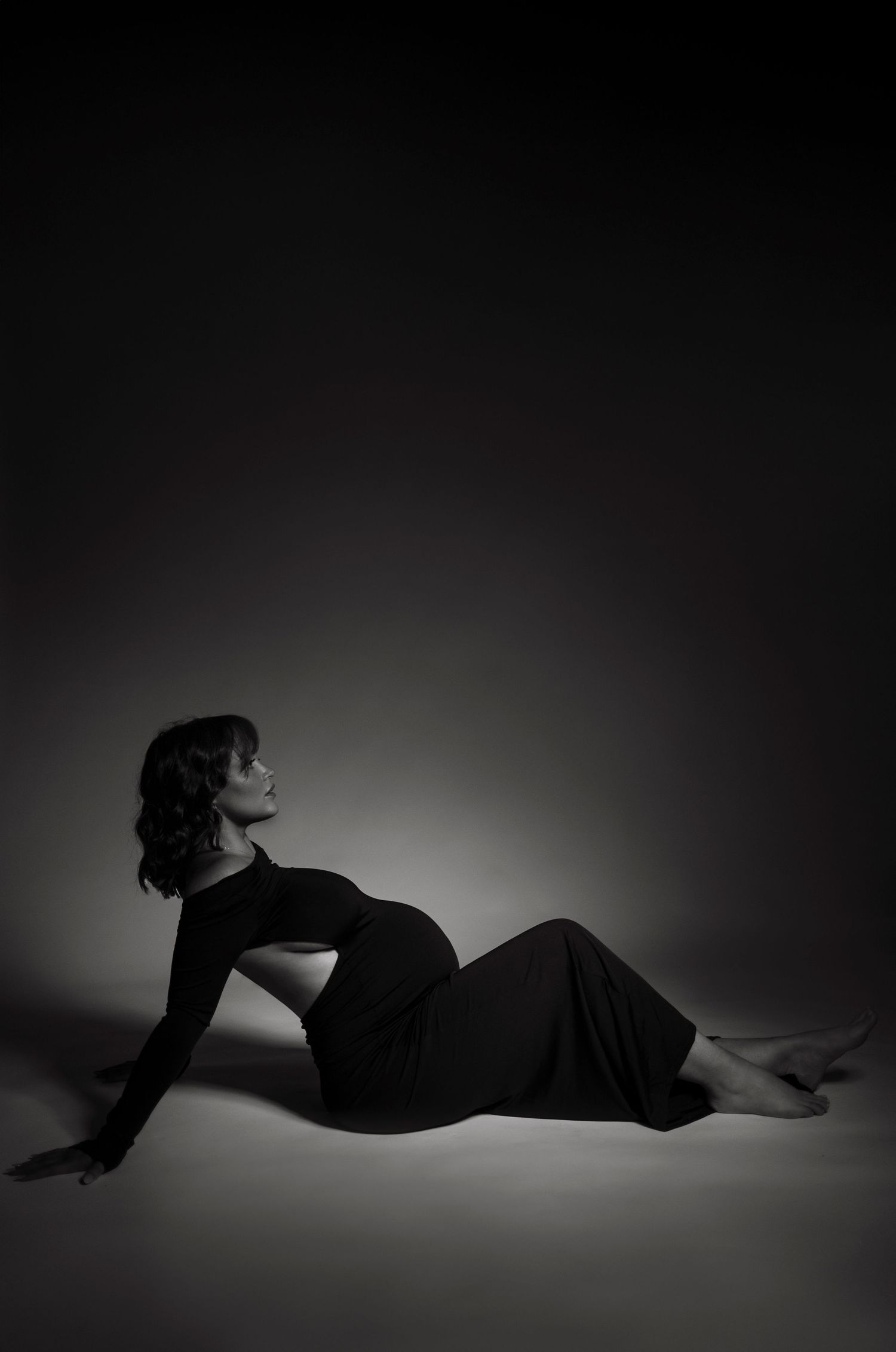 Silhouette of person in black dress reclining dramatically against dark background.