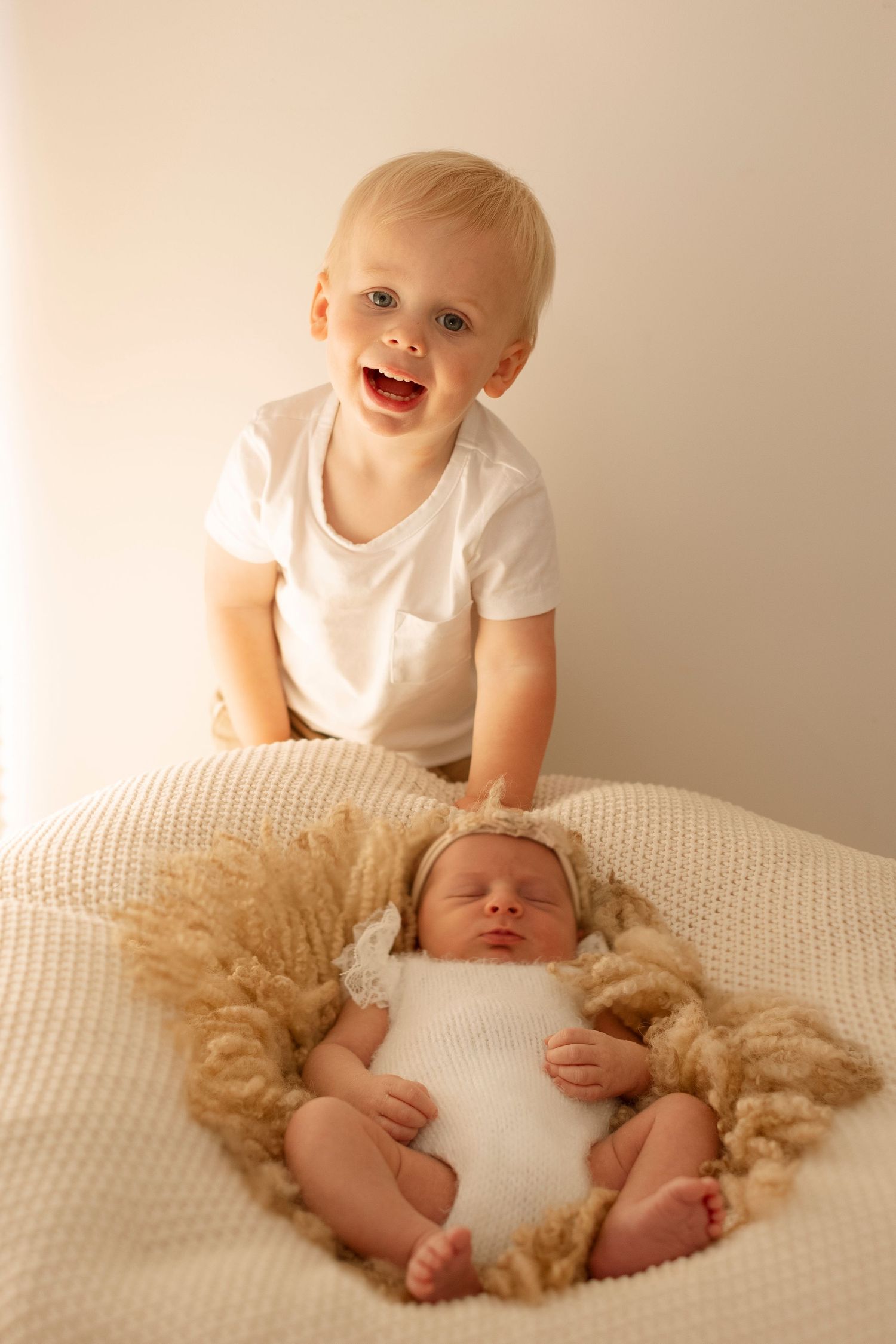 Four sequential photos showing a baby in white clothing playing with a fluffy beige blanket on a light-colored bed.