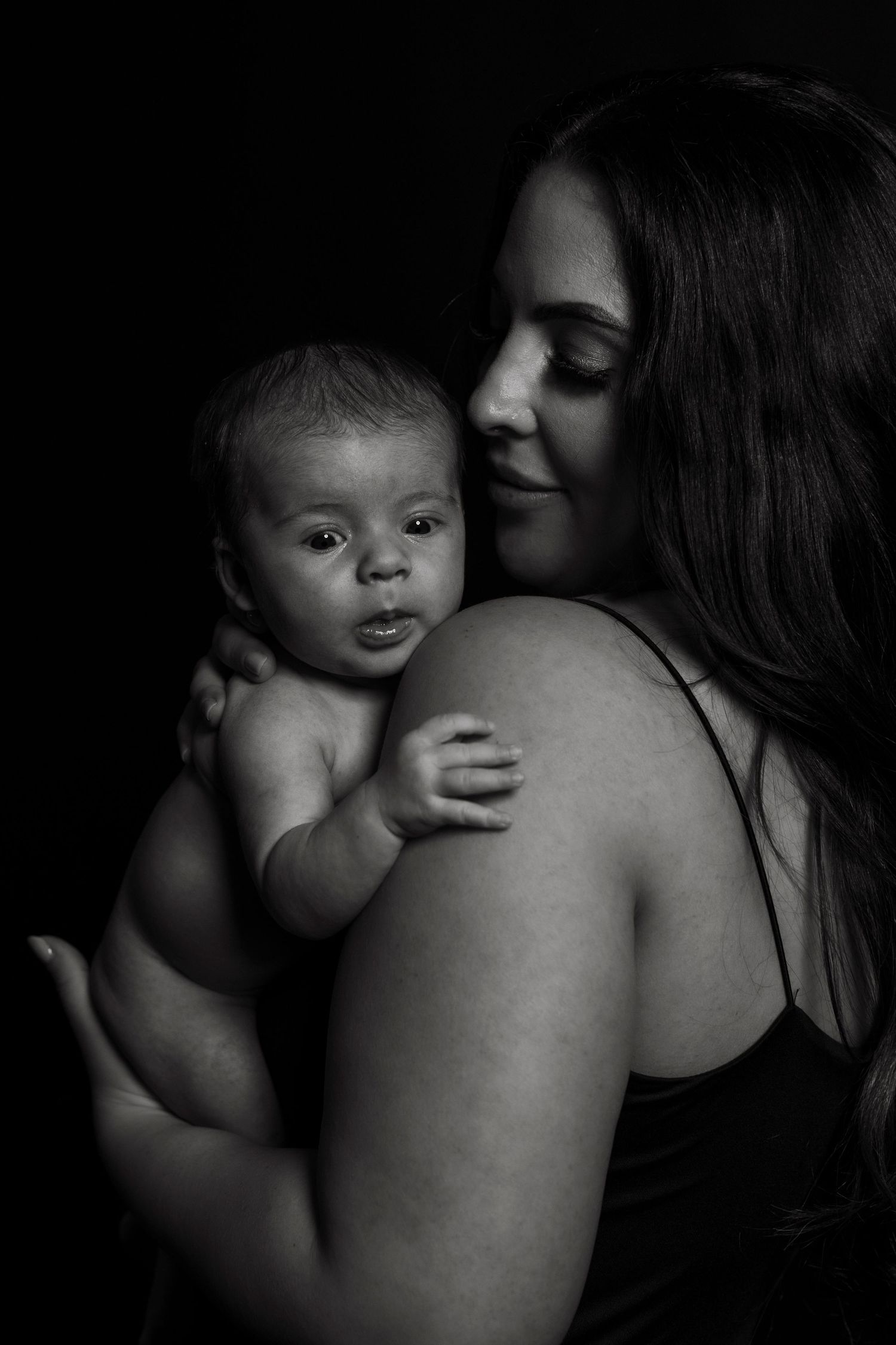 Dramatic black and white portrait of mother and infant in intimate embrace.