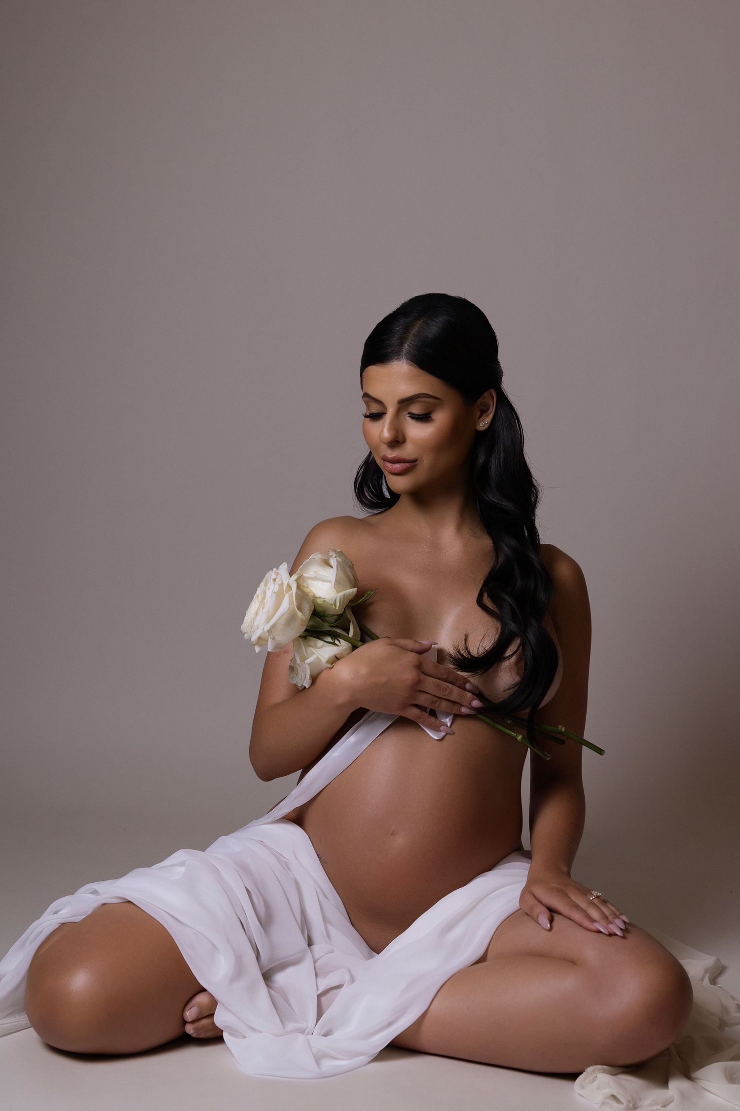 Artistic maternity photo series showing a pregnant woman in white fabric against neutral backdrop.