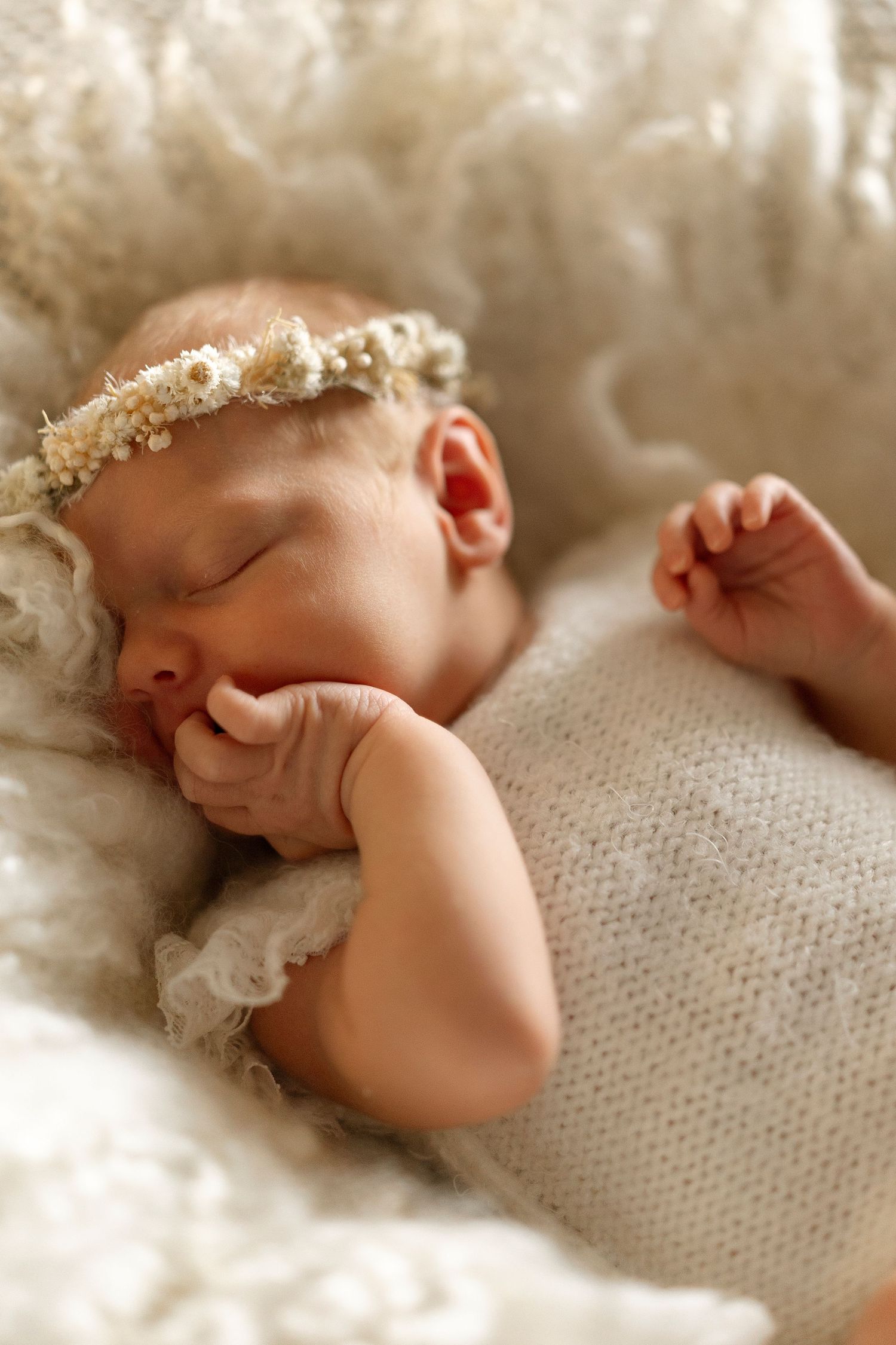 Sleeping newborn baby wrapped in textured knit blanket with soft sepia toned lighting.