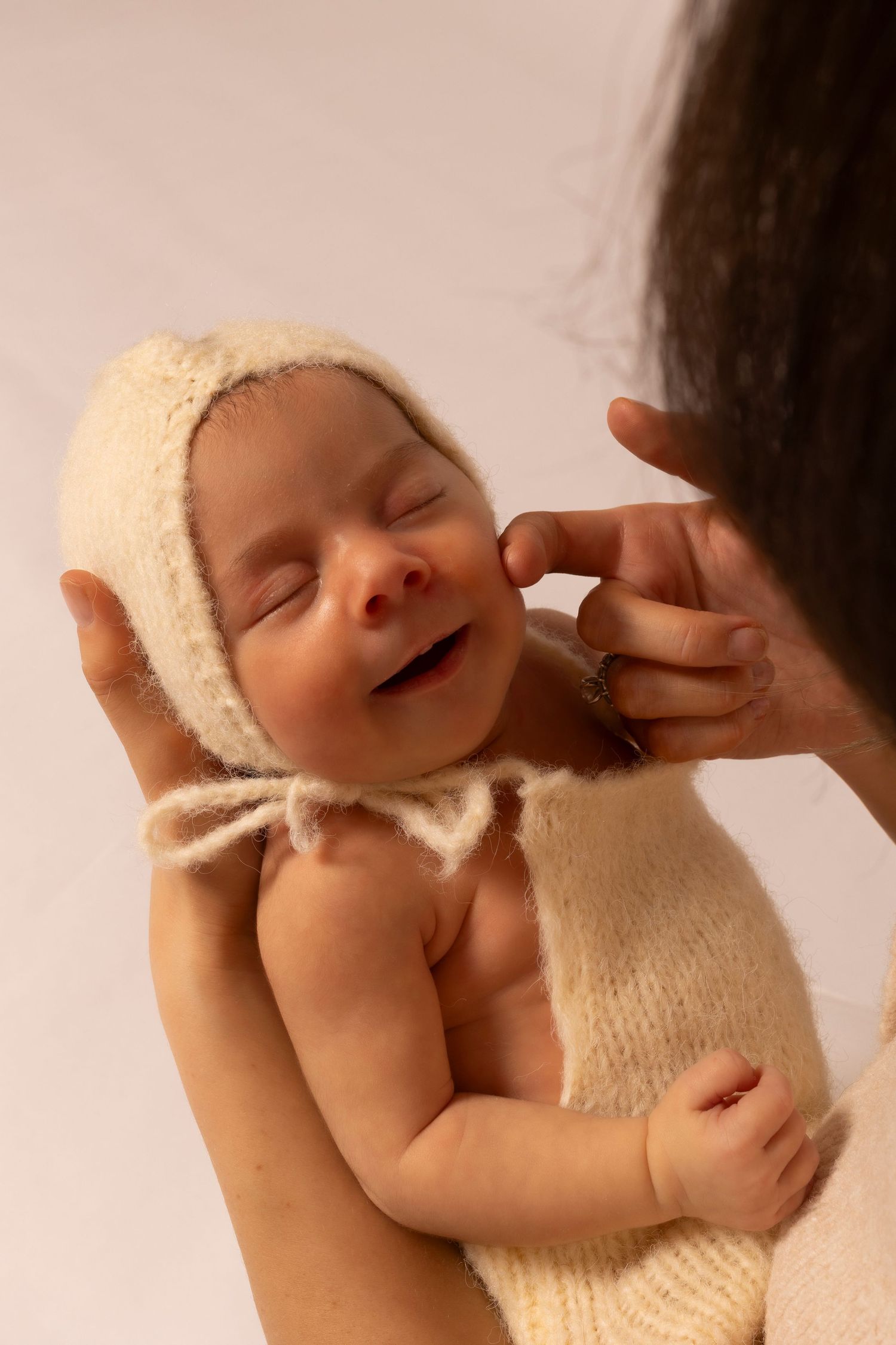 A sleeping newborn baby wrapped in a soft cream-colored knit blanket being gently cradled.