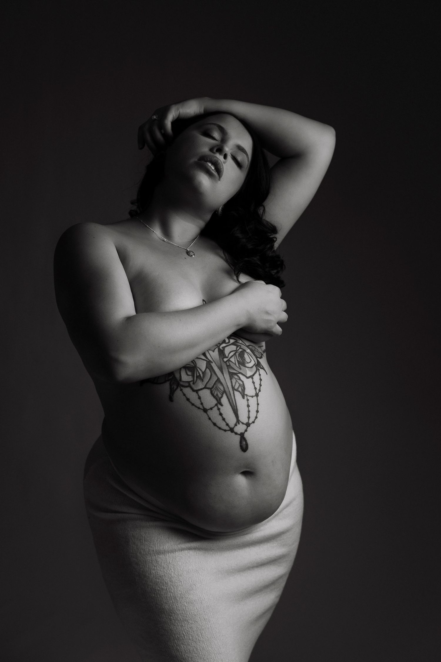 Artistic black and white portrait showcasing a curvy figure in intimate lighting against dark background.