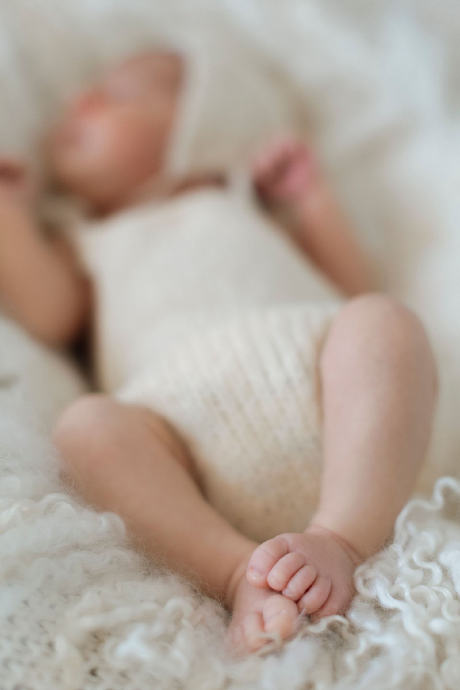 A sleeping baby wrapped in soft white blankets with tiny hand visible resting on lace fabric.