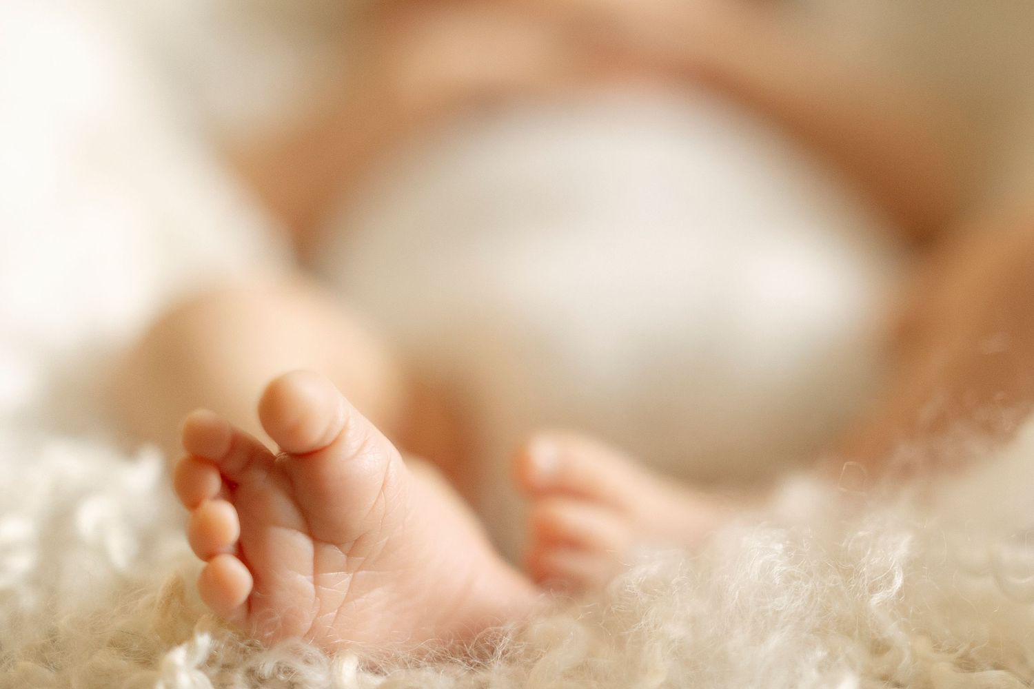 A tiny baby foot emerges from soft white blankets in a tender newborn photography portrait.