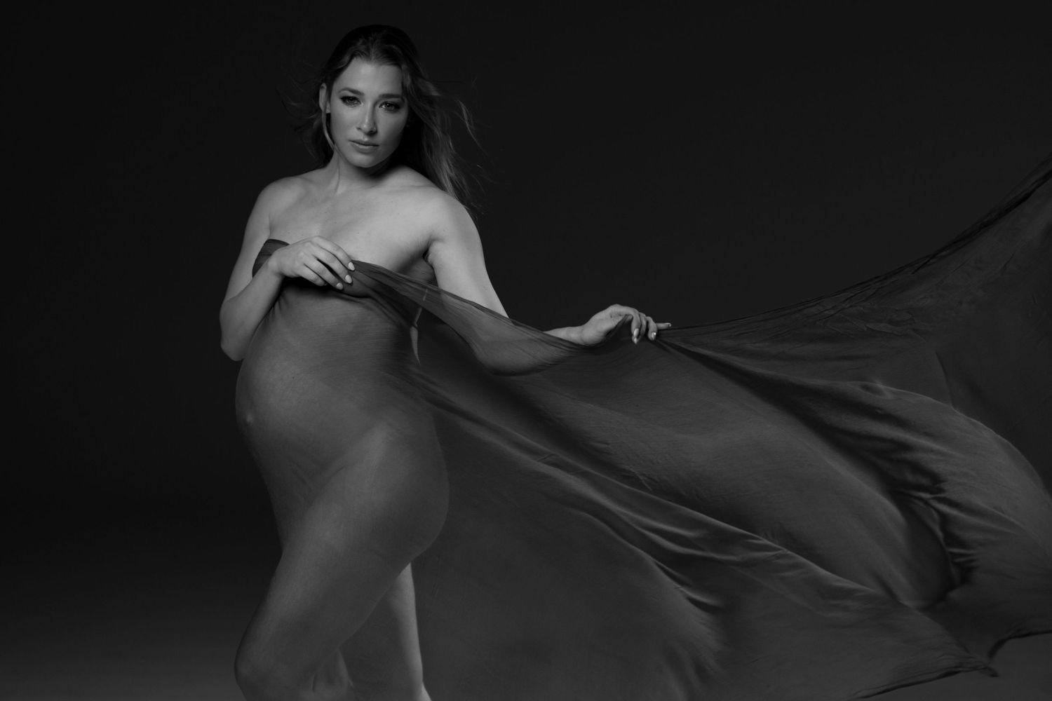 Elegant black and white maternity photos with flowing fabric creating dramatic movement.