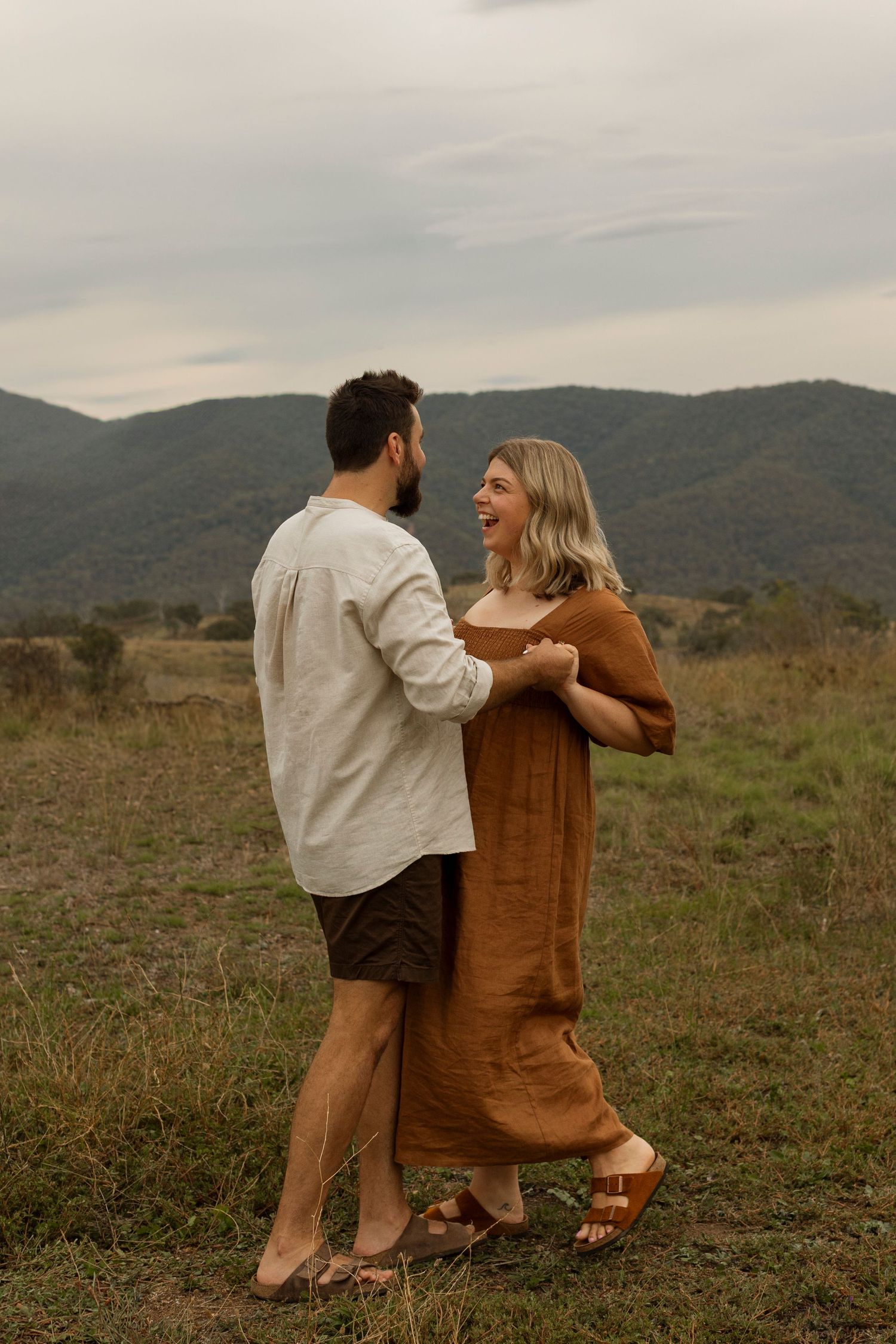 Couple sharing tender moments together against mountainous backdrop in warm sunlight.