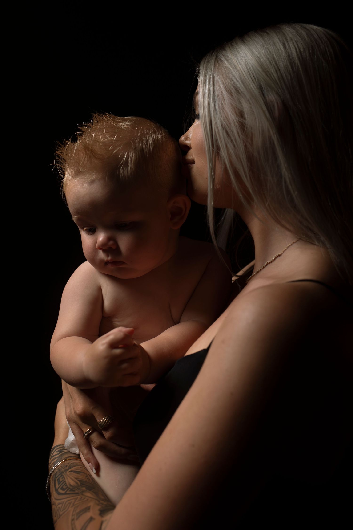 Artistic low key photography capturing tender maternal moments in dramatic lighting.