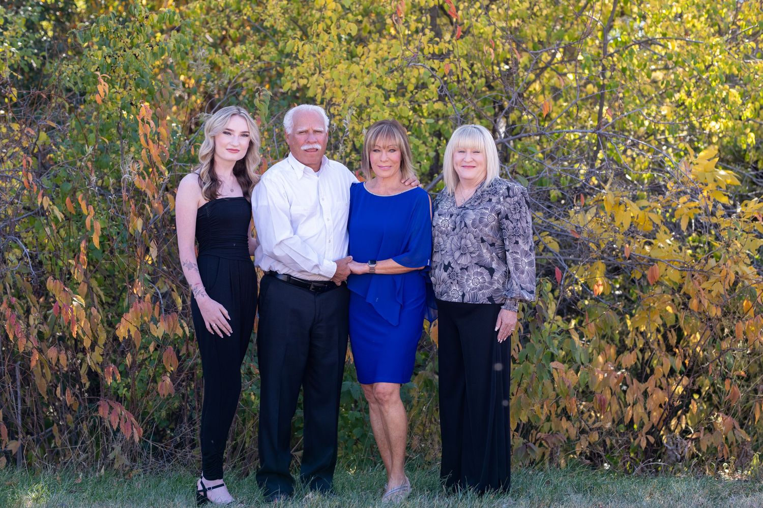Family group poses outdoors against autumn foliage backdrop in coordinated outfits.