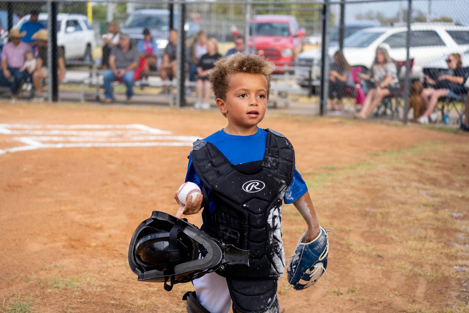 A young baseball player in blue and black protective gear runs on a dirt baseball field during a game.