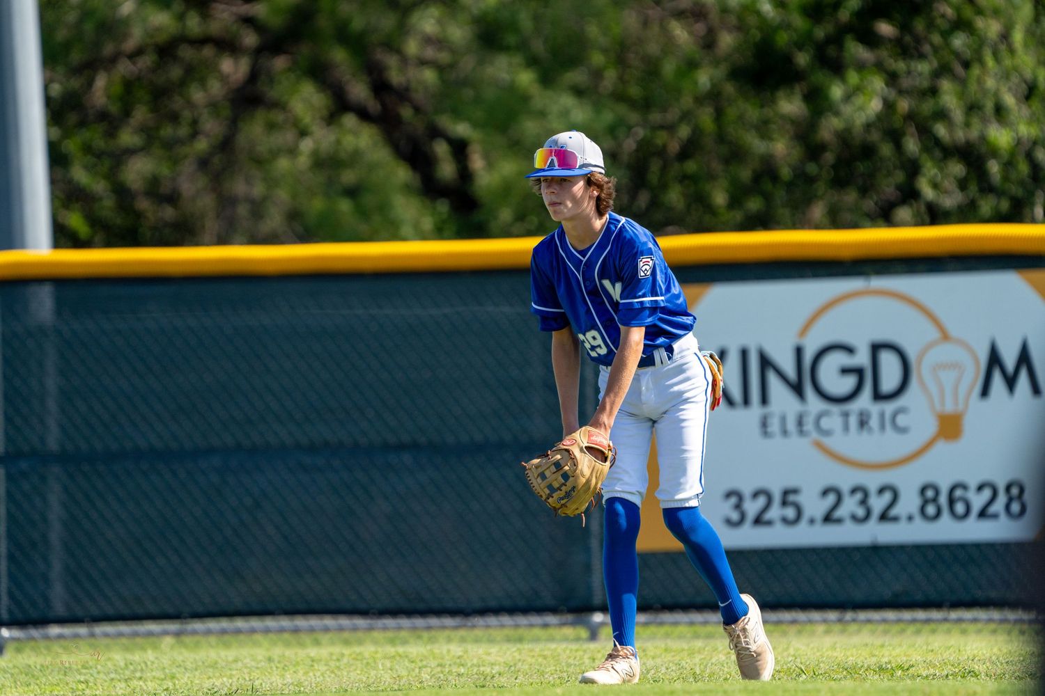 Baseball player in blue uniform stands ready in fielding position on baseball diamond during daytime game.