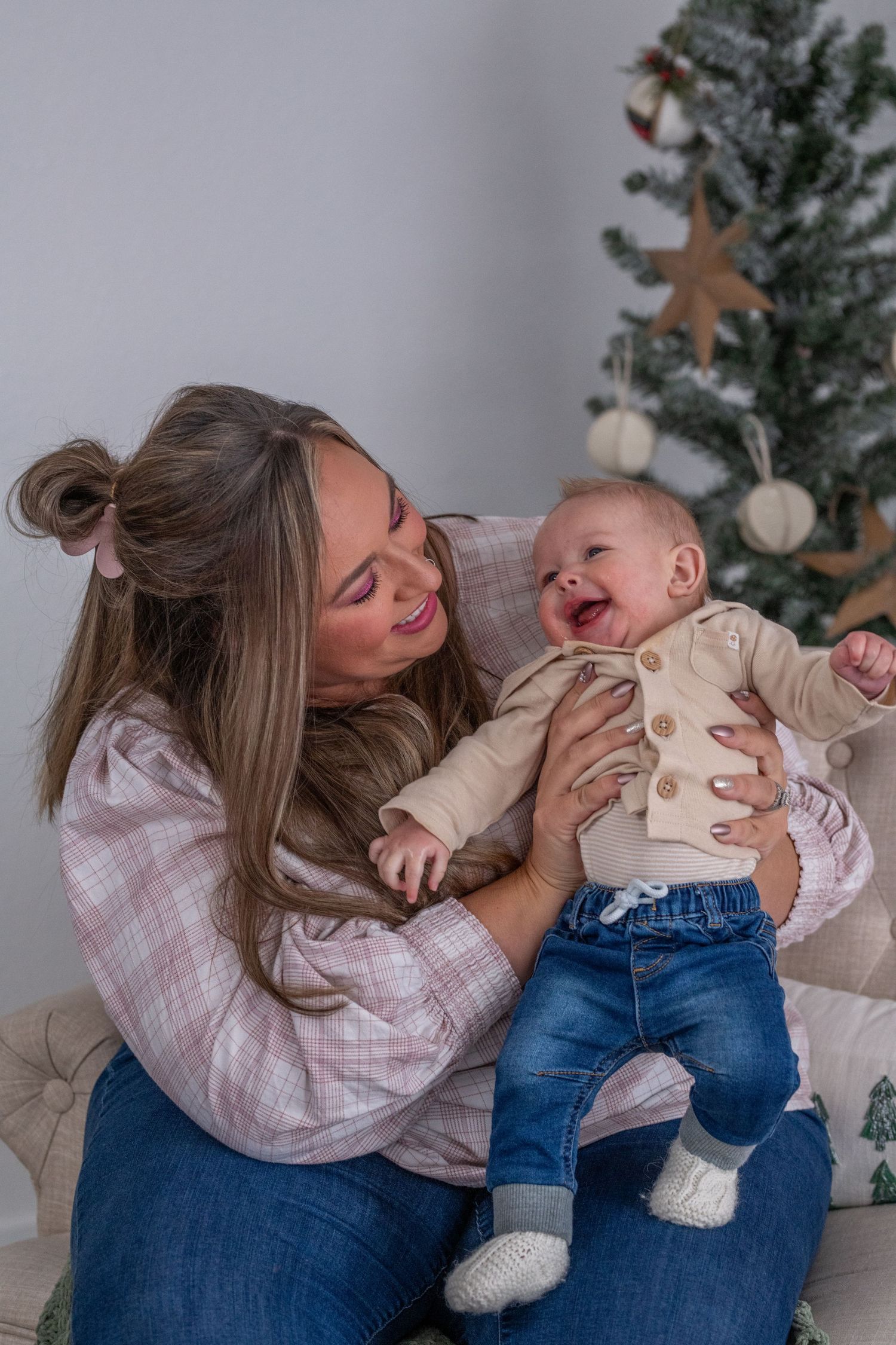 A joyful baby and parent share a heartwarming moment in front of a Christmas tree.