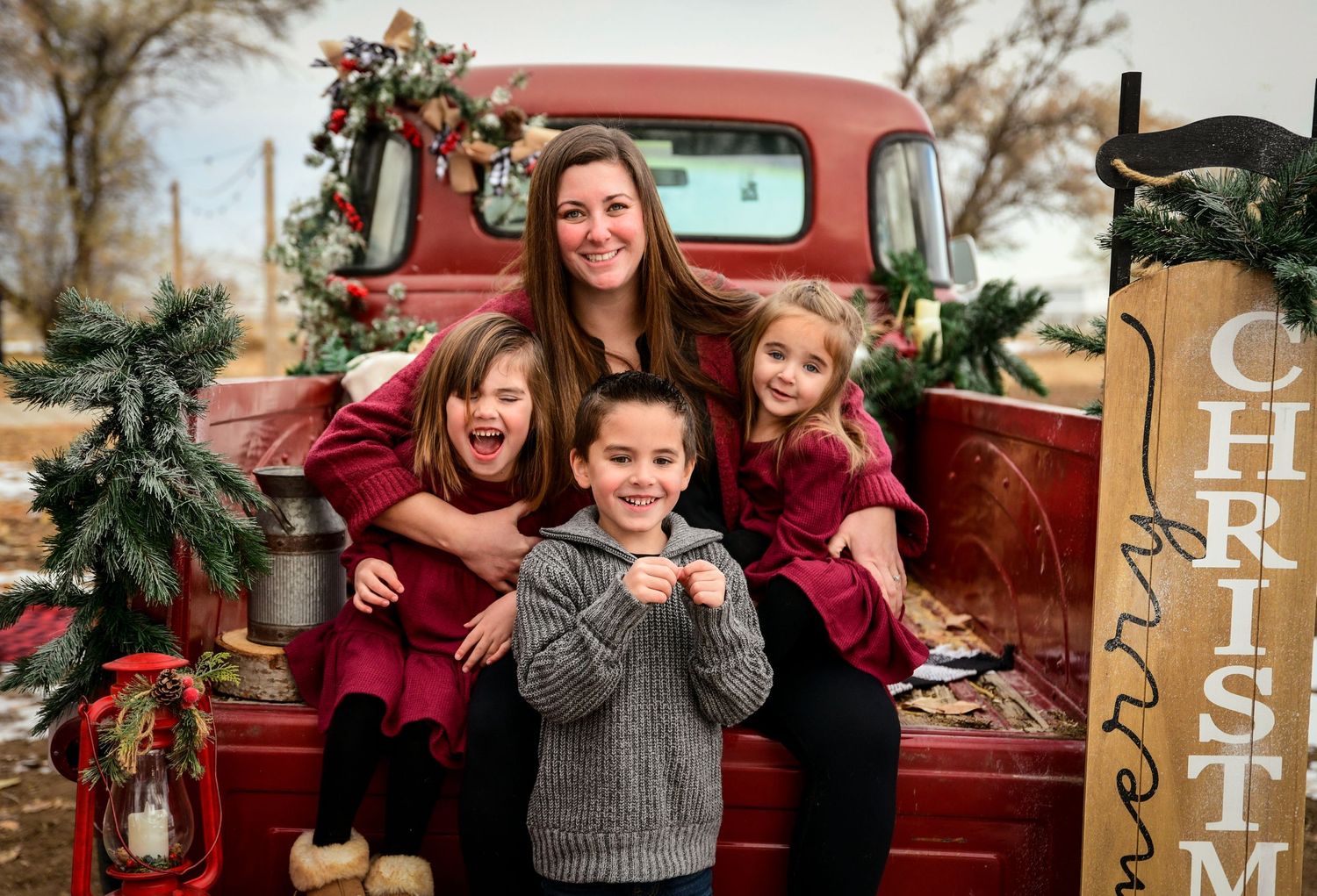 Christmas portrait with vintage red truck decorated with garland and family in coordinating outfits.