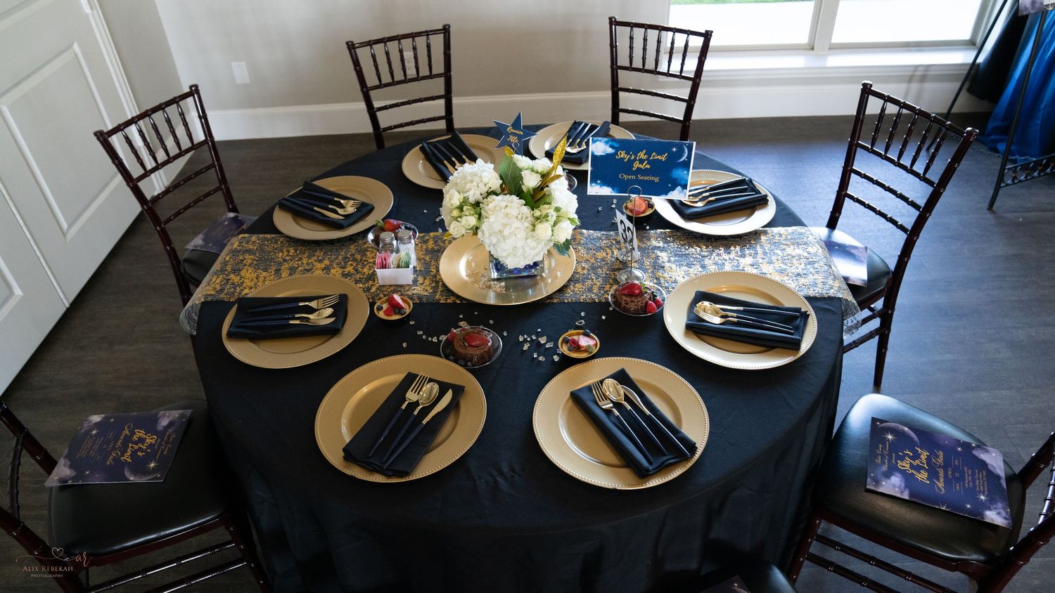 Elegant table setting with gold chargers and black linens at formal dinner event.