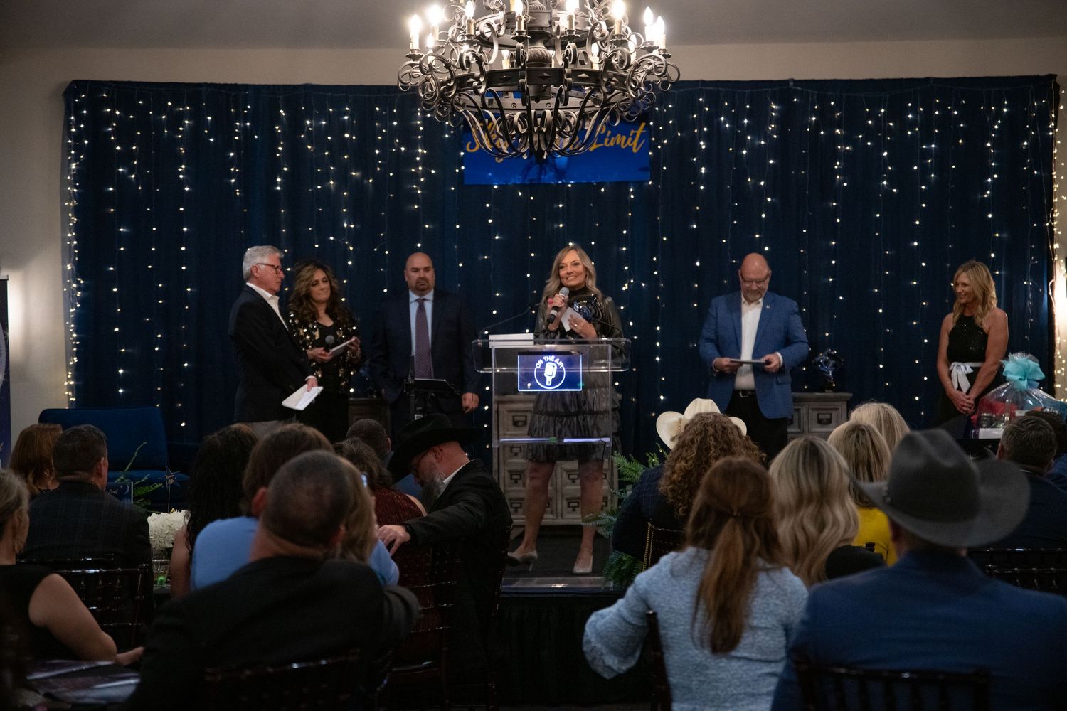 An awards ceremony setup with chandelier and twinkle light backdrop during an evening event.