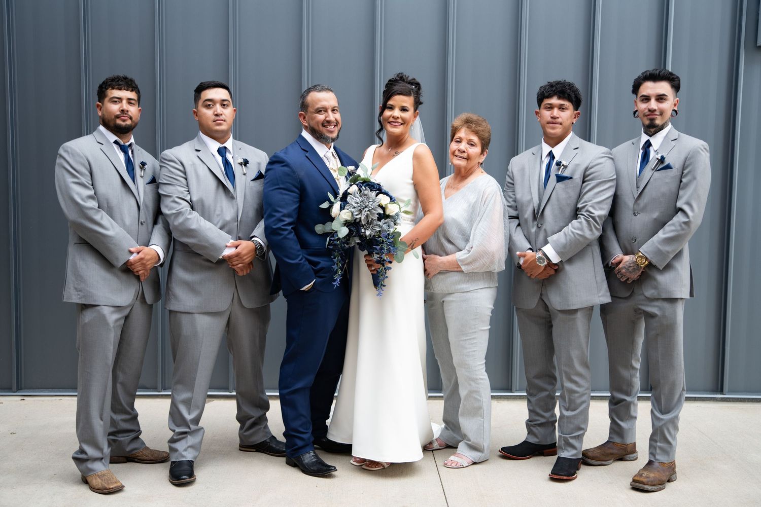 Formal wedding party portrait with groomsmen in light grey suits against dark wall.