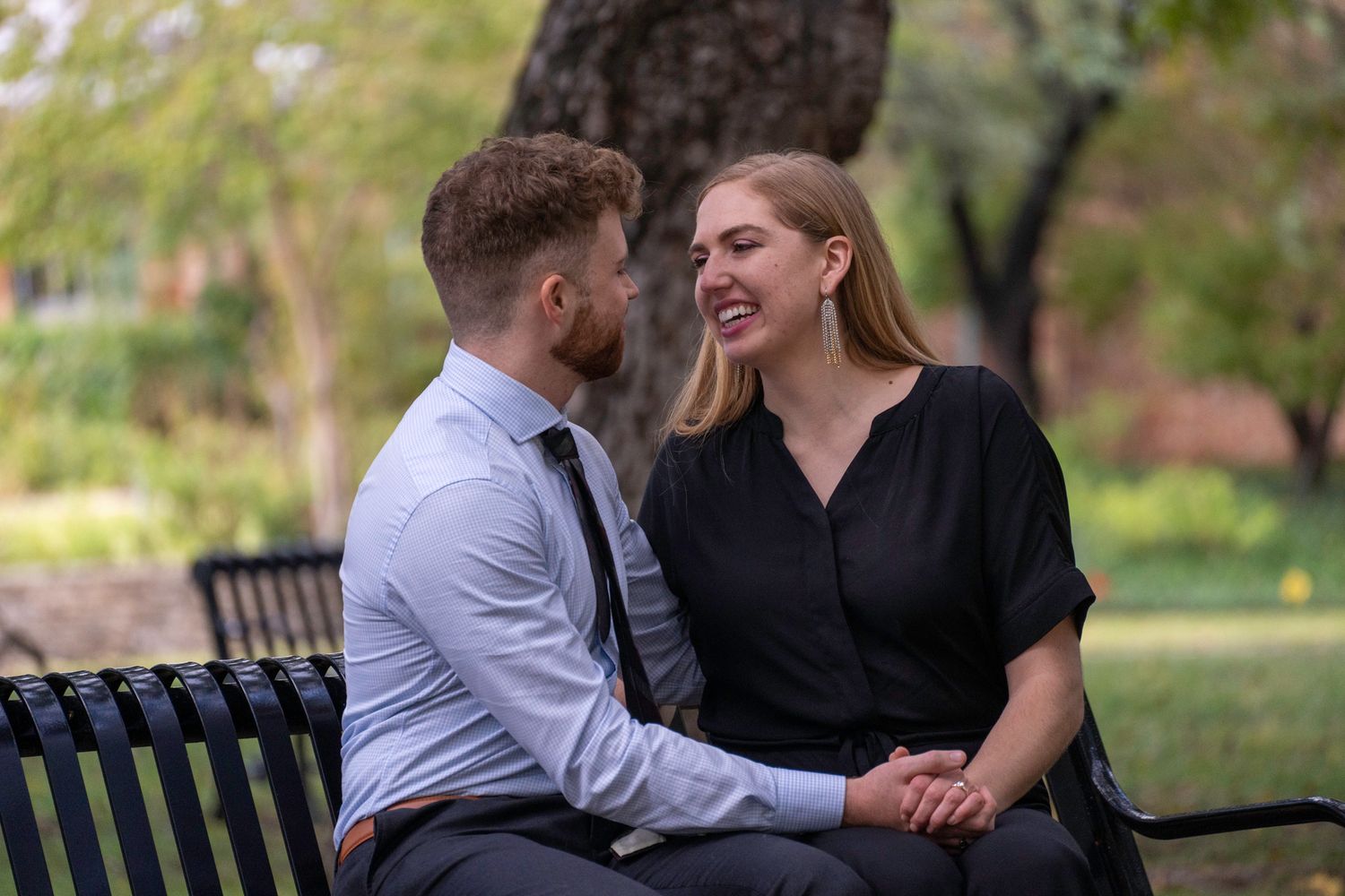 Couple laughing and embracing while sitting on park benches during an outdoor photography session.