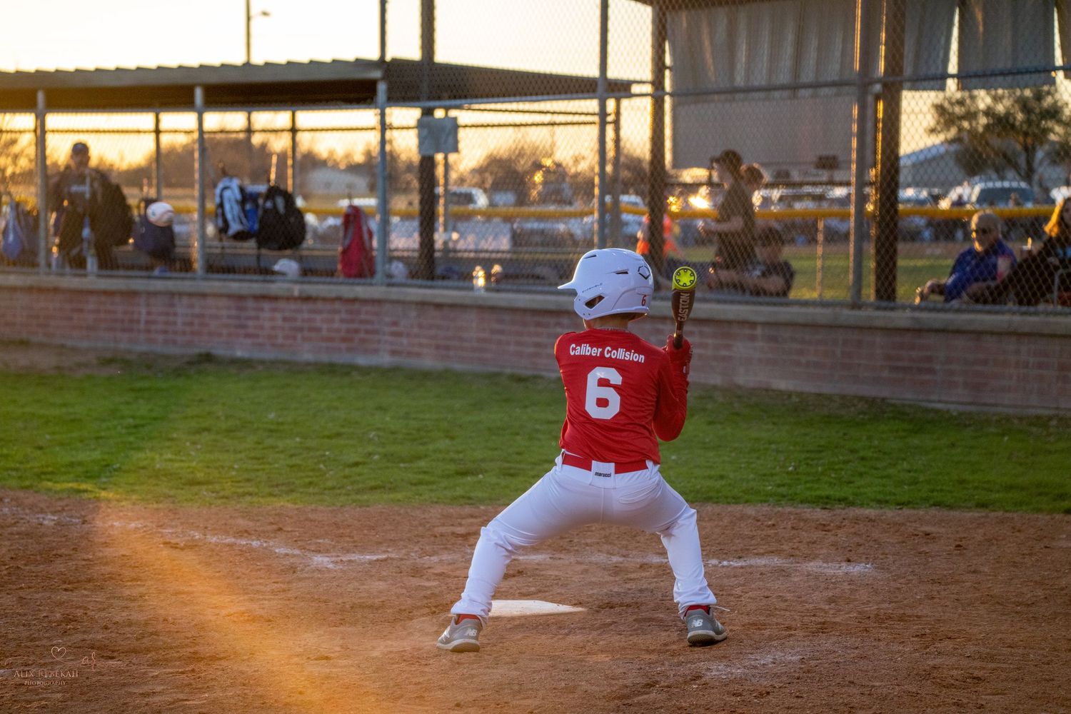 A baseball player wearing number 6 in red stands in batting position at home plate during golden hour.
