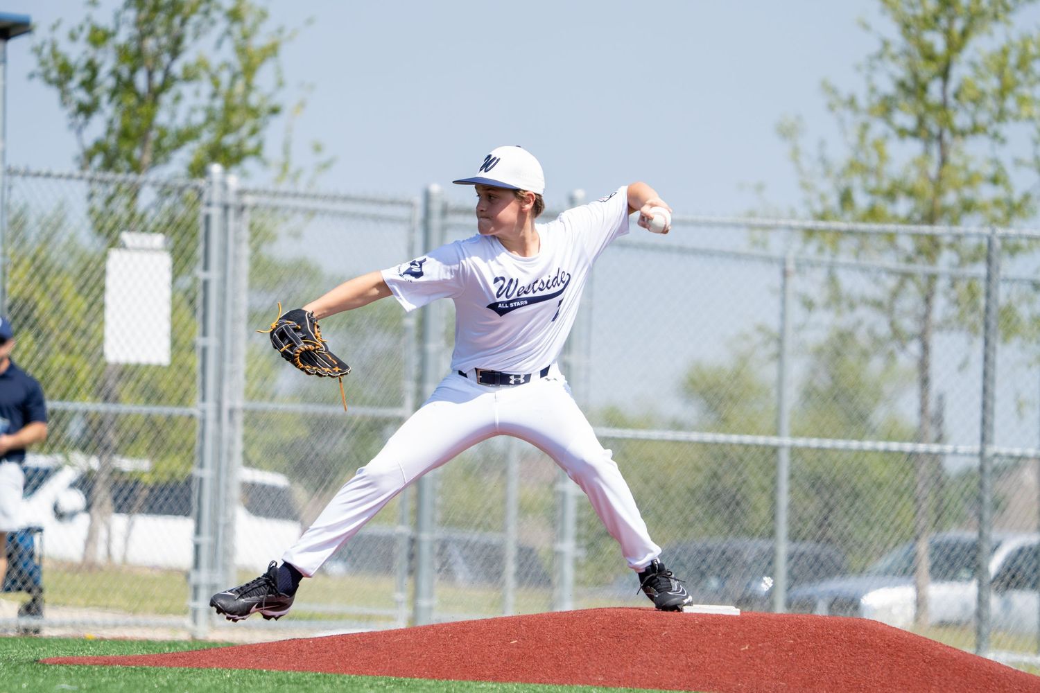 Baseball pitcher in white uniform throwing pitch from pitching mound in outdoor game.