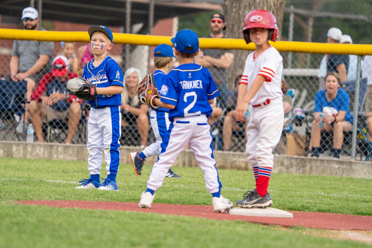 A baseball player slides into base while another player in a blue uniform attempts to make a defensive play.
