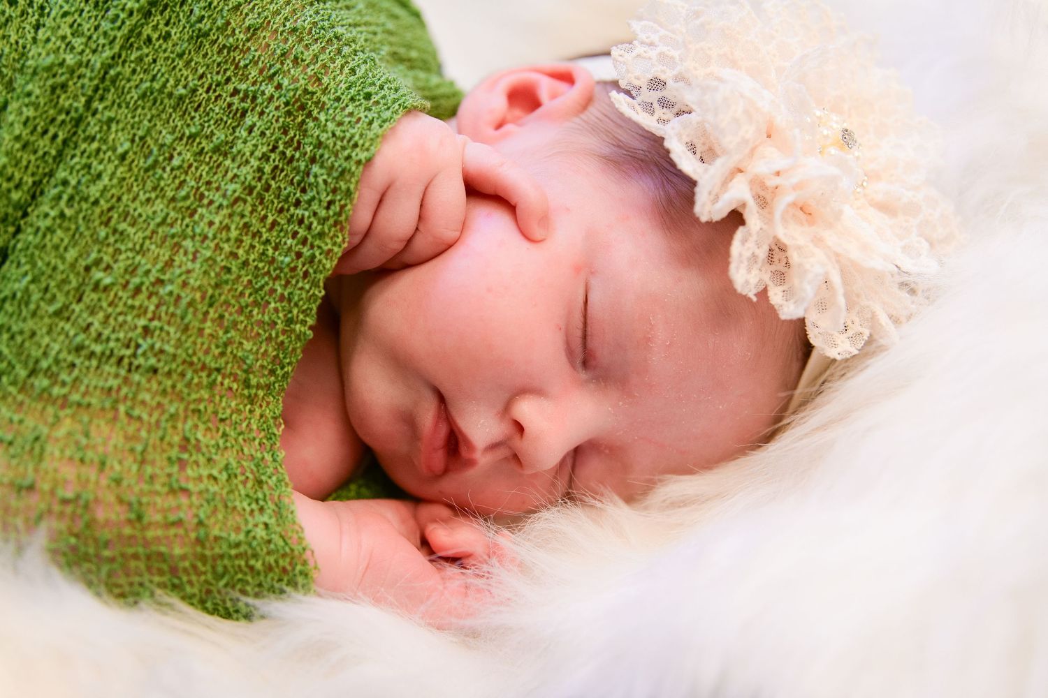 Peaceful sleeping newborn wrapped in green knit blanket with lace headband.