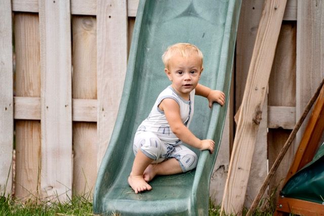 Toddler climbing on green playground slide in backyard.