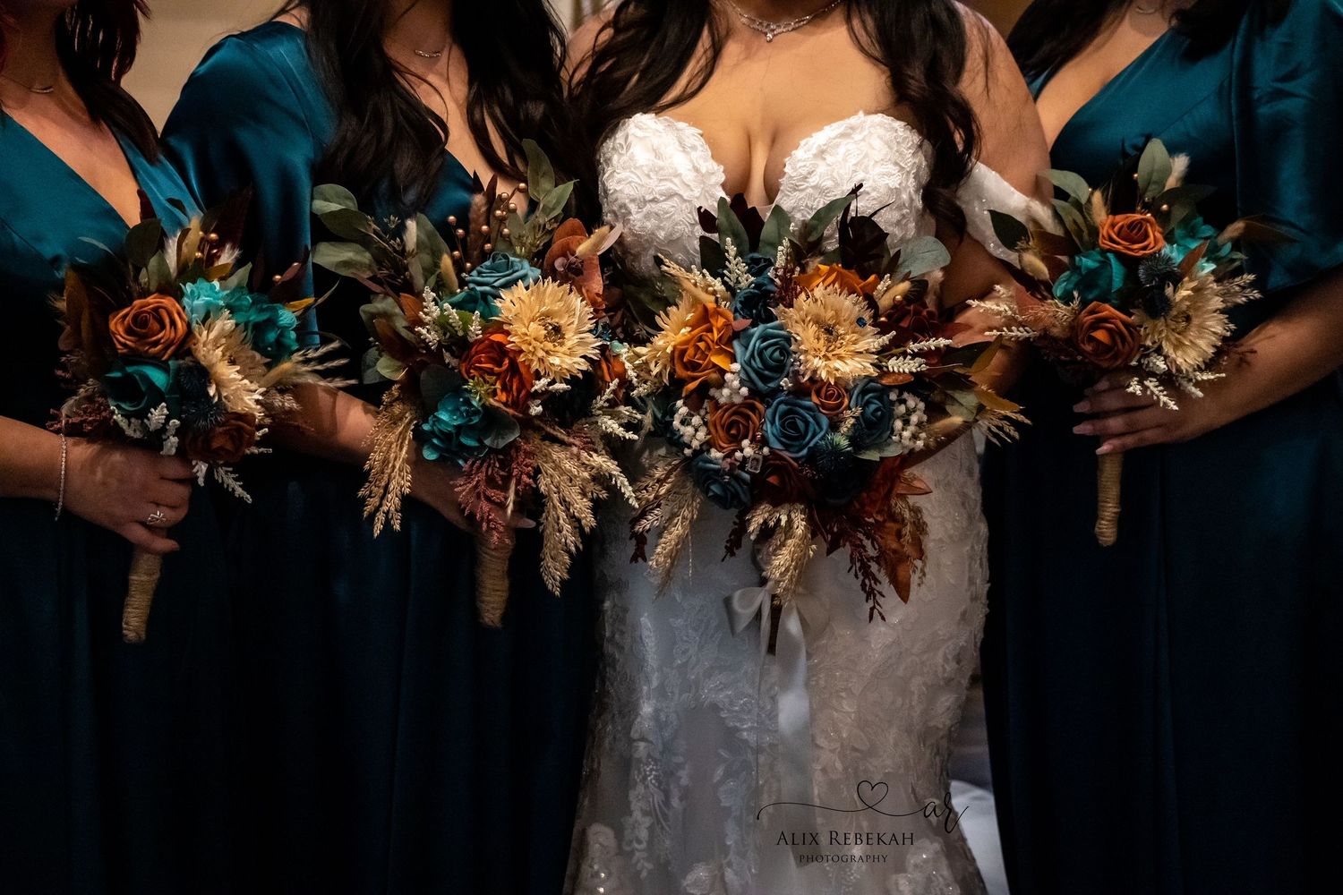 Wedding party holds rustic autumn bouquets featuring dried flowers and feathers against teal dresses and white bridal gown.