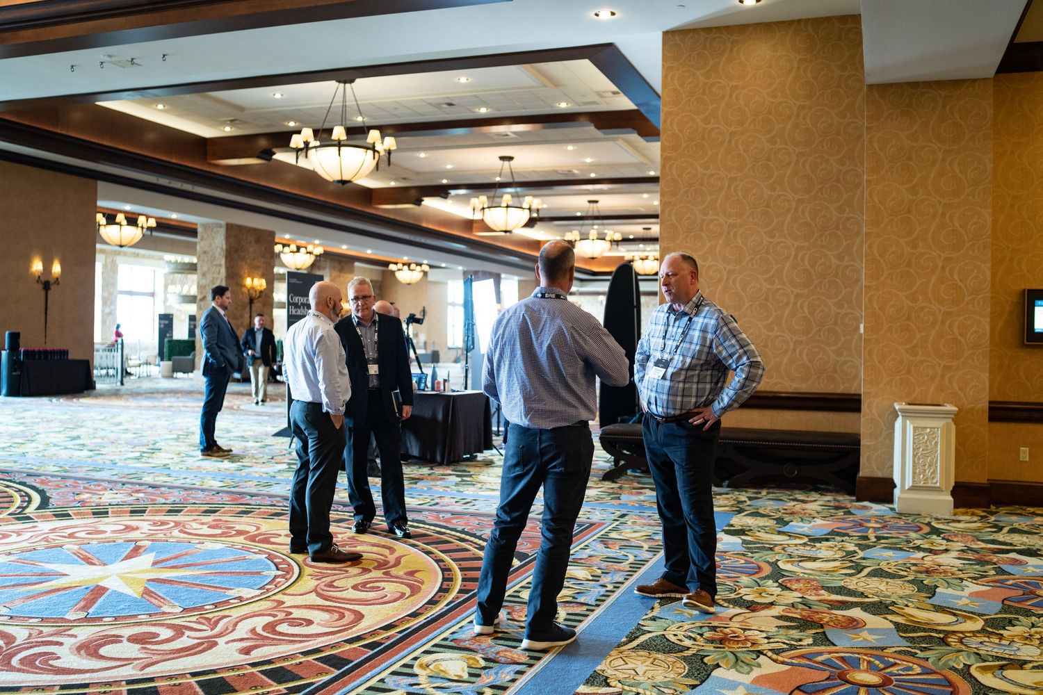 Professional attendees networking in a hotel conference space with ornate carpeting.