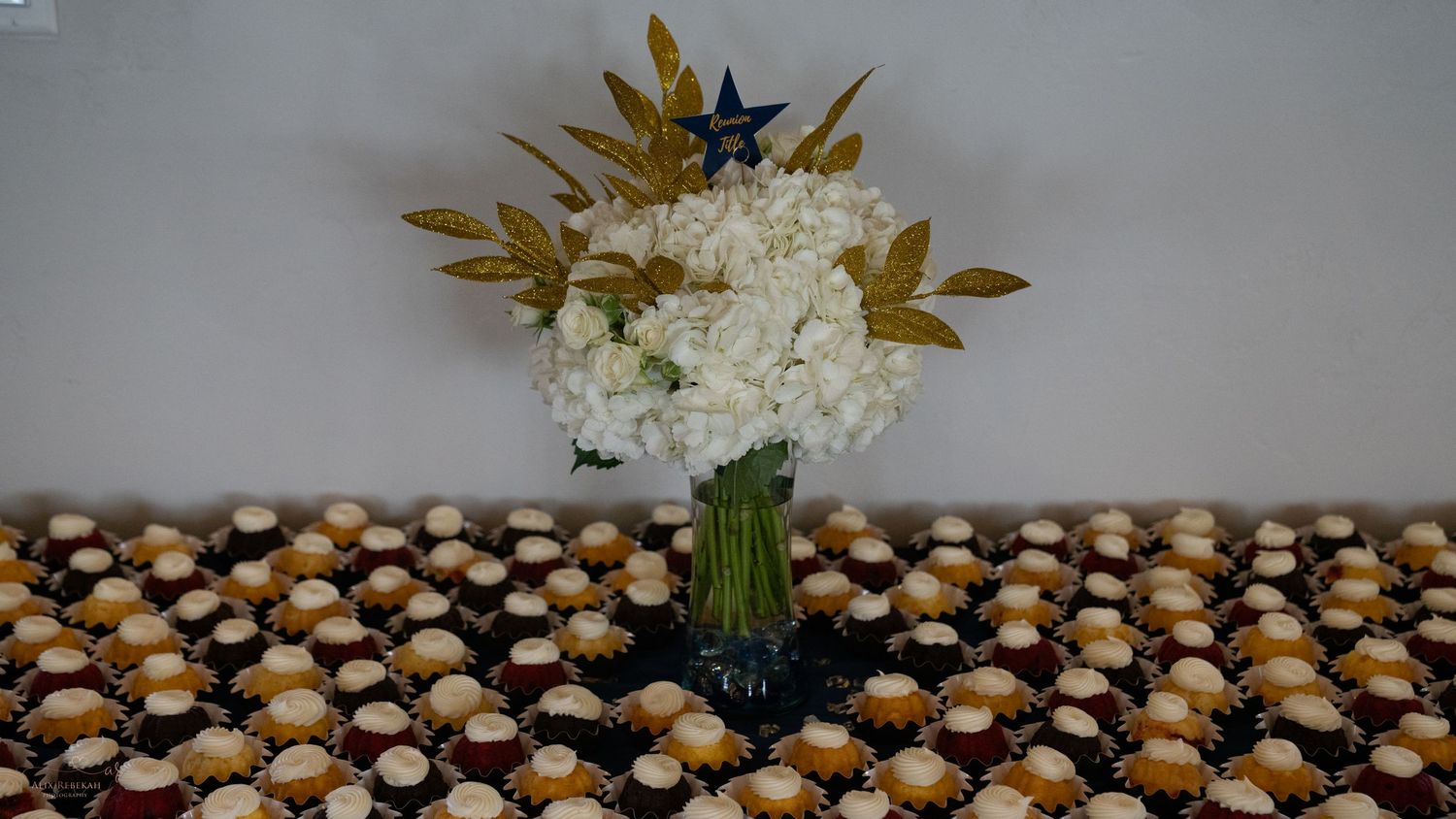 White hydrangea centerpiece displayed among rows of decorated dessert favors.