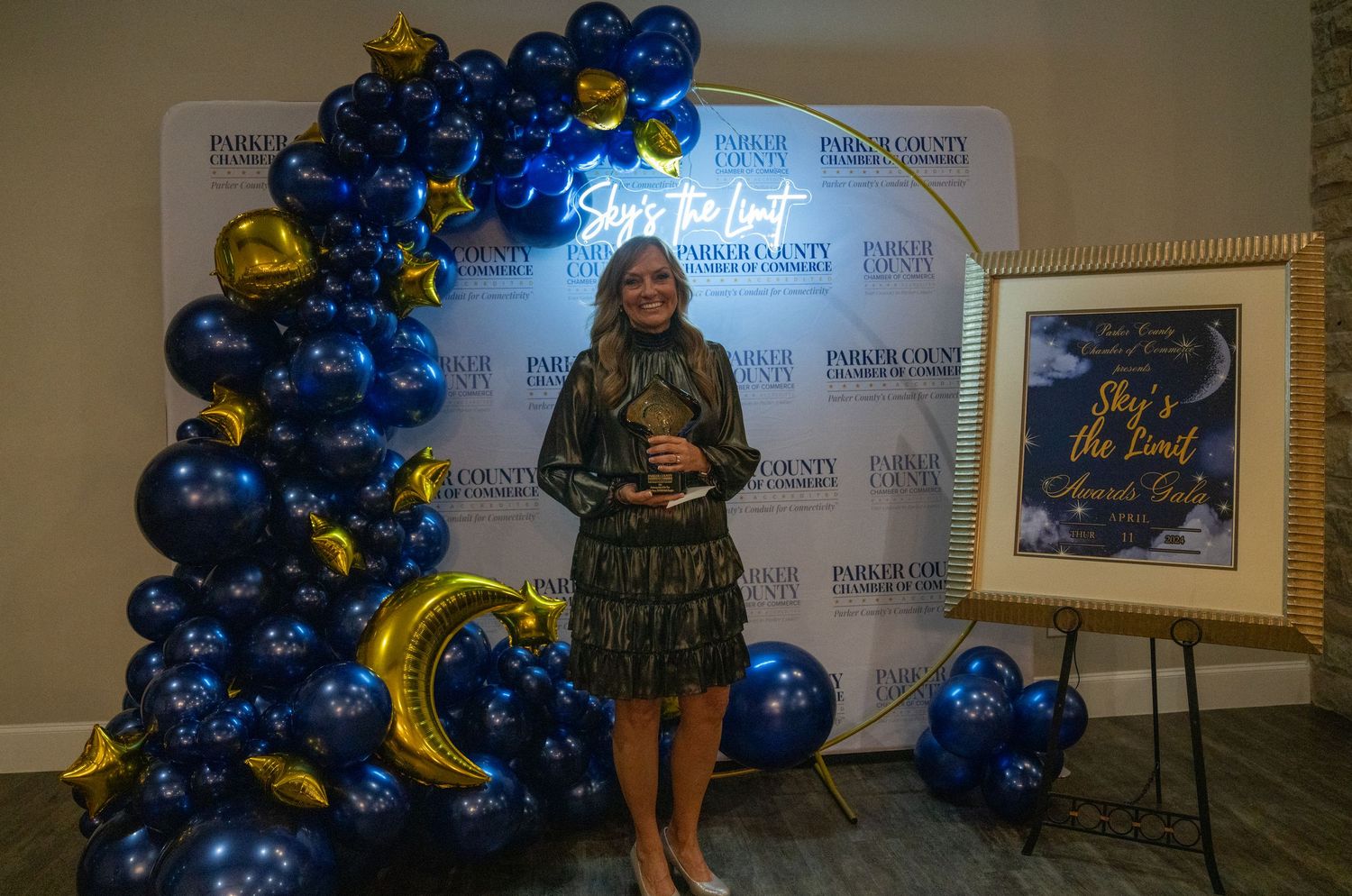 An award recipient poses in front of a decorative balloon display at a formal event.