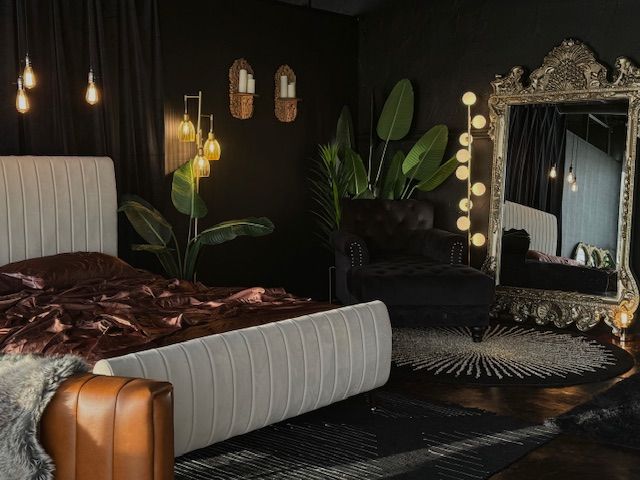 Moody bedroom interior with upholstered bed, ornate mirror, and hanging pendant lights against dark walls.