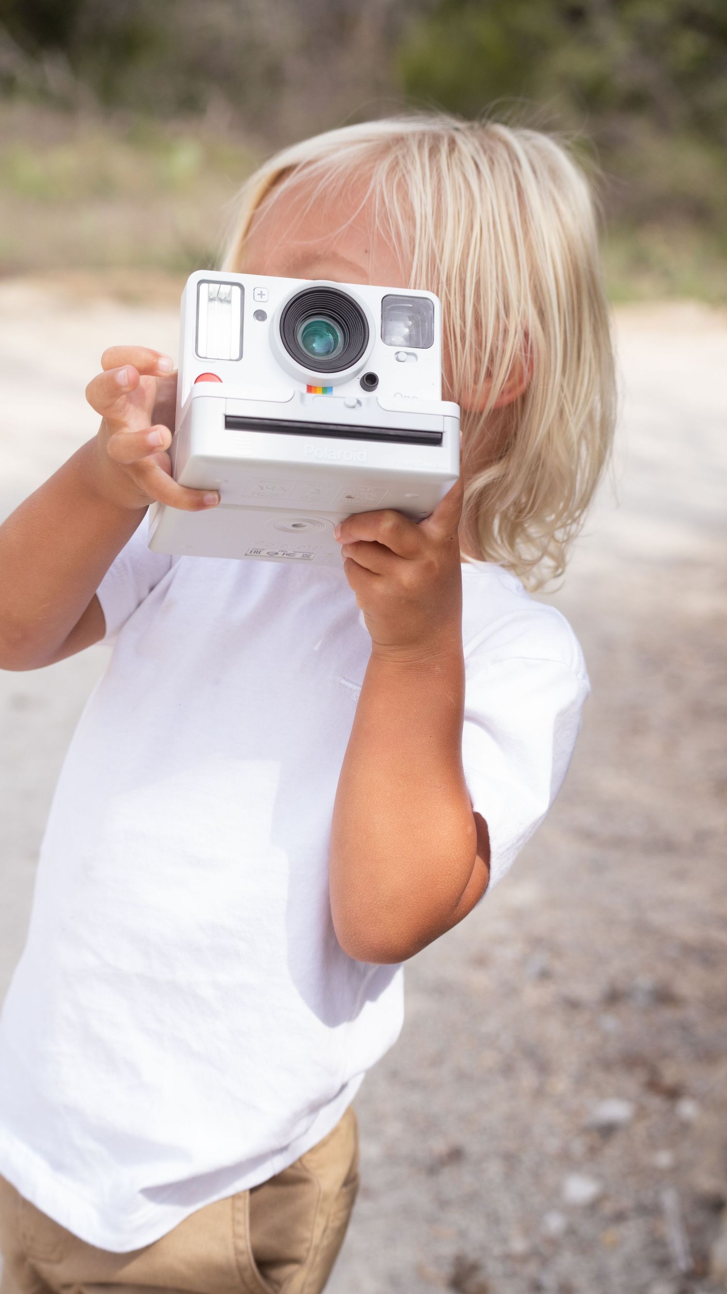 A sequence shows a child in a white shirt holding up a polaroid camera to take a photo in an outdoor setting.