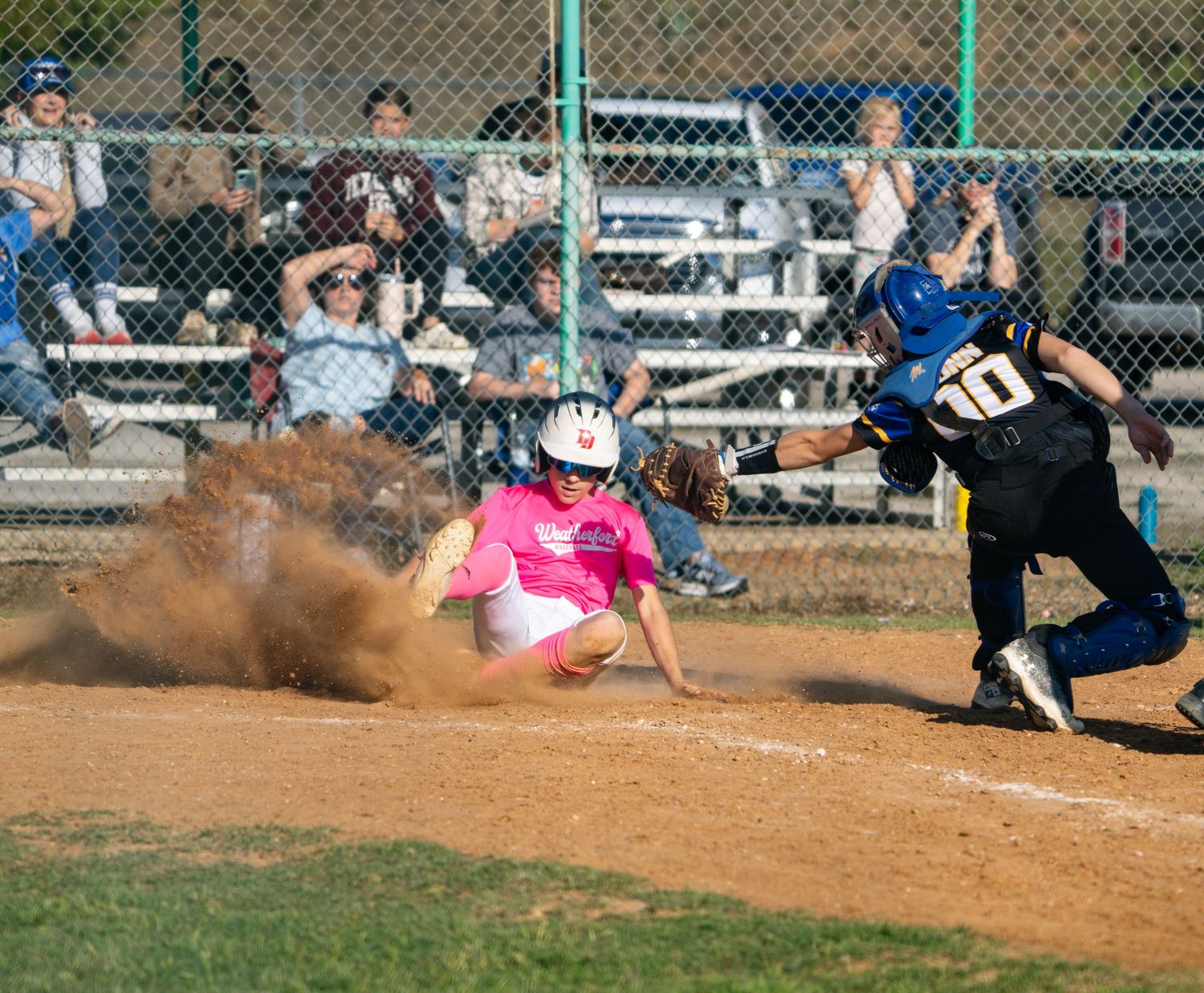 A dramatic baseball play unfolds at home plate as dust flies during an intense sliding attempt to score.