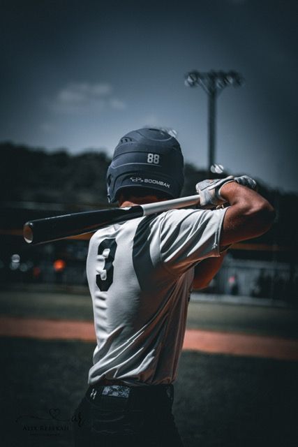 Baseball player in uniform number 3 taking a batting stance against a moody evening sky with field lights.