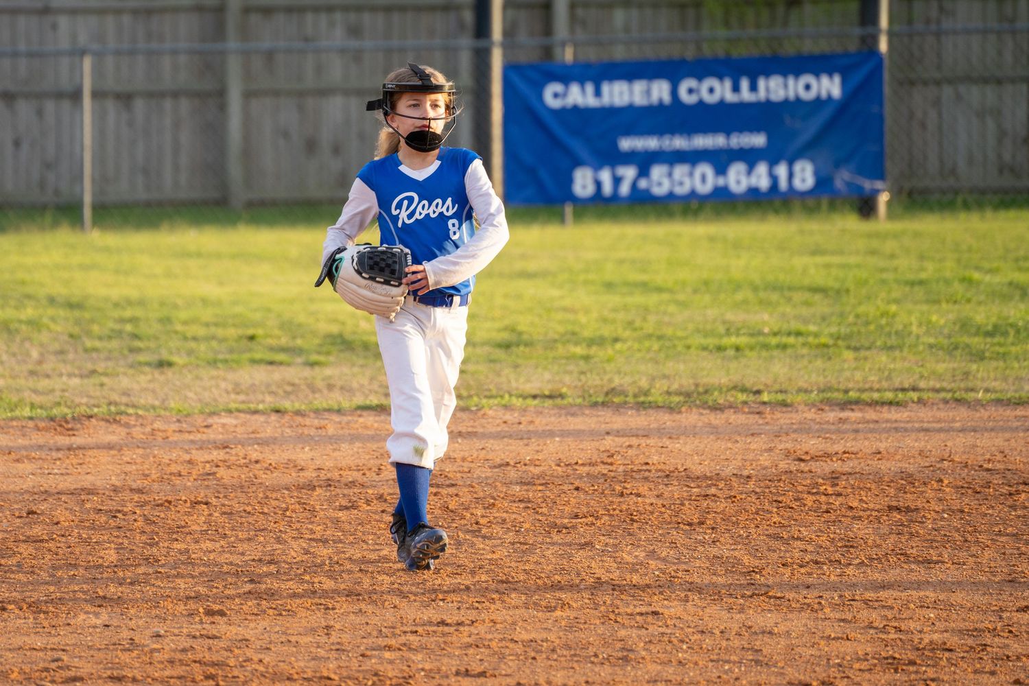 Youth baseball player in blue and white uniform running on a dirt infield during a game at a local baseball field.