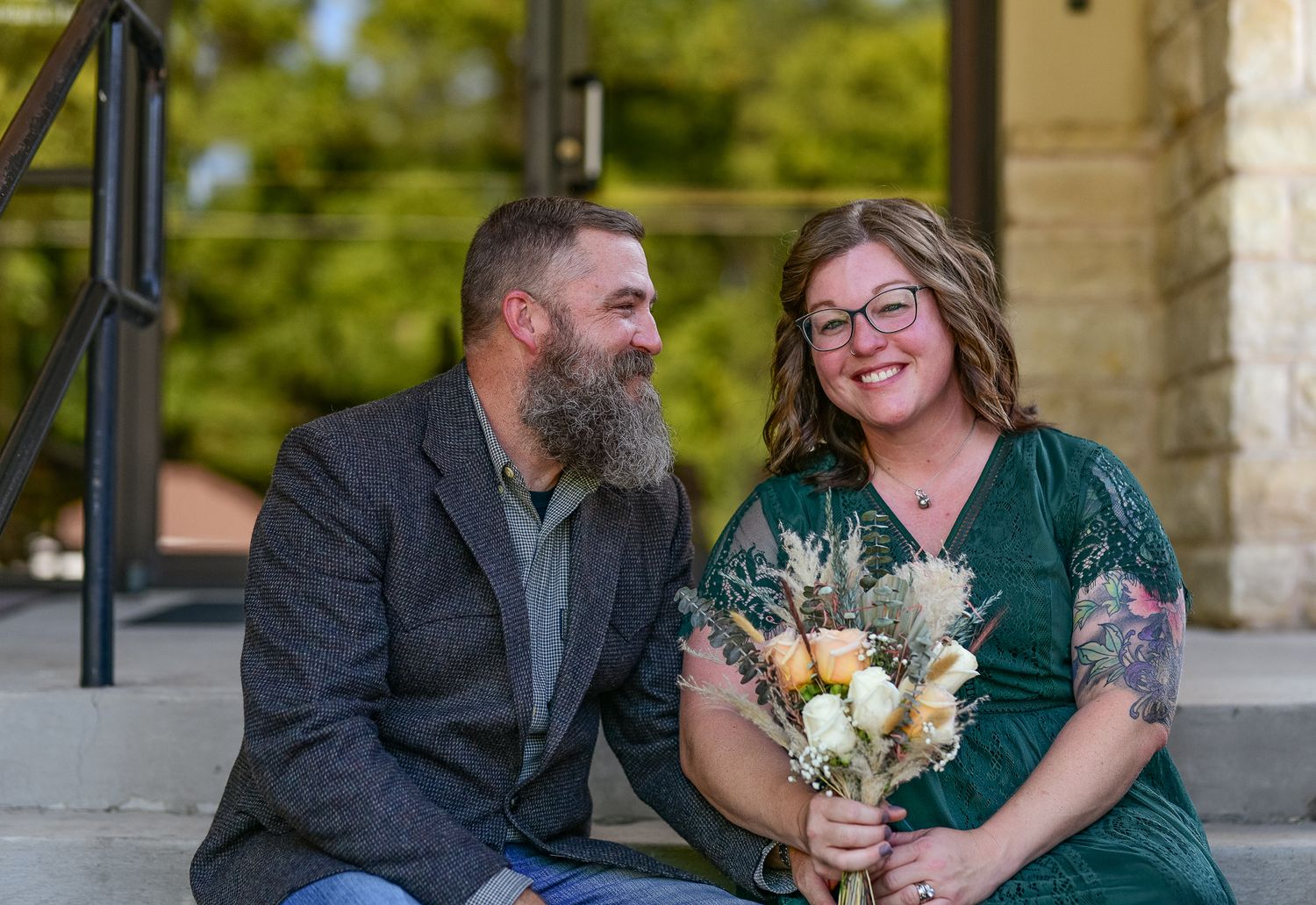 Couple sitting on stone steps, sharing a joyful moment with dried floral bouquet.