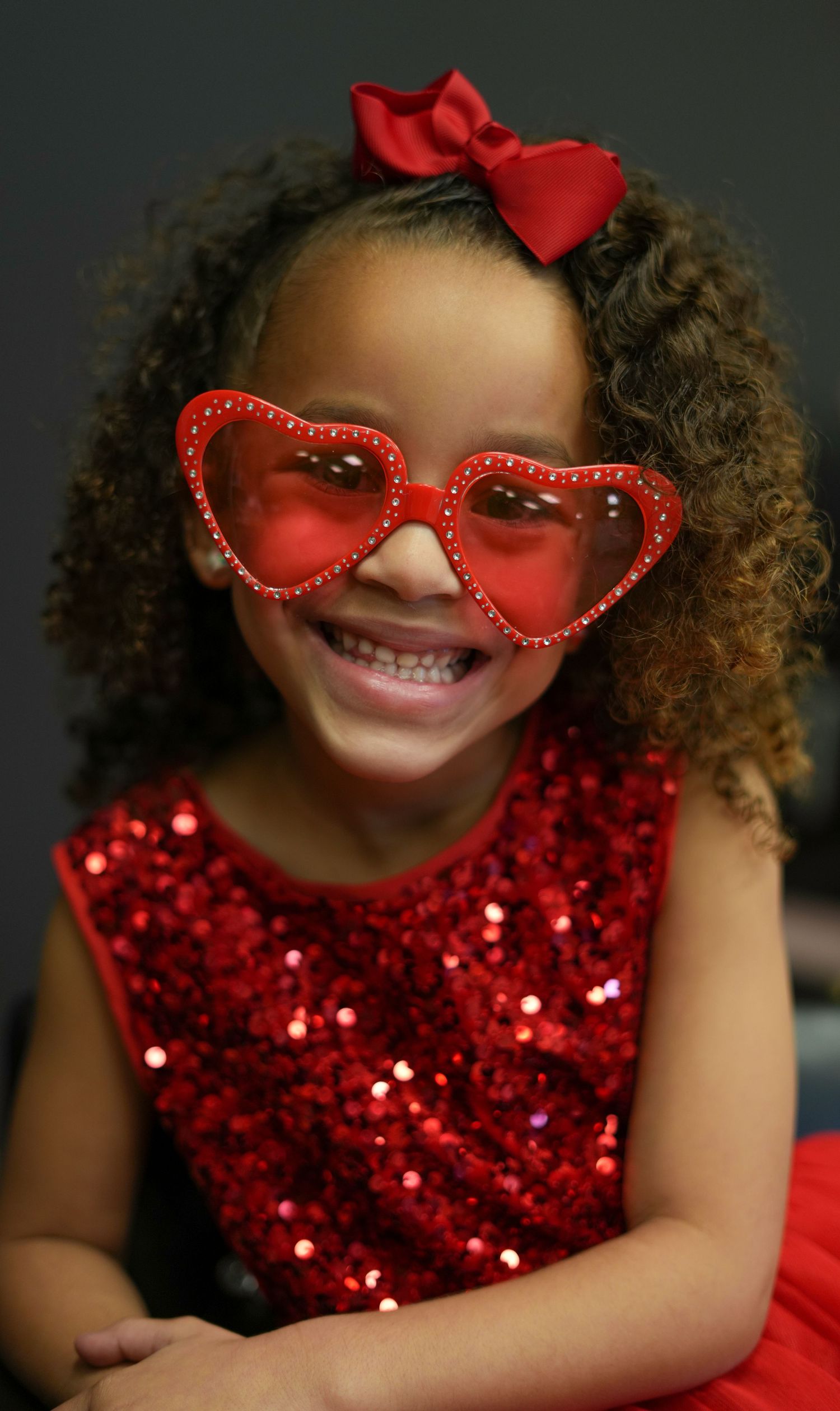 Joyful expression captured while wearing red sequin dress and decorative heart-shaped glasses.