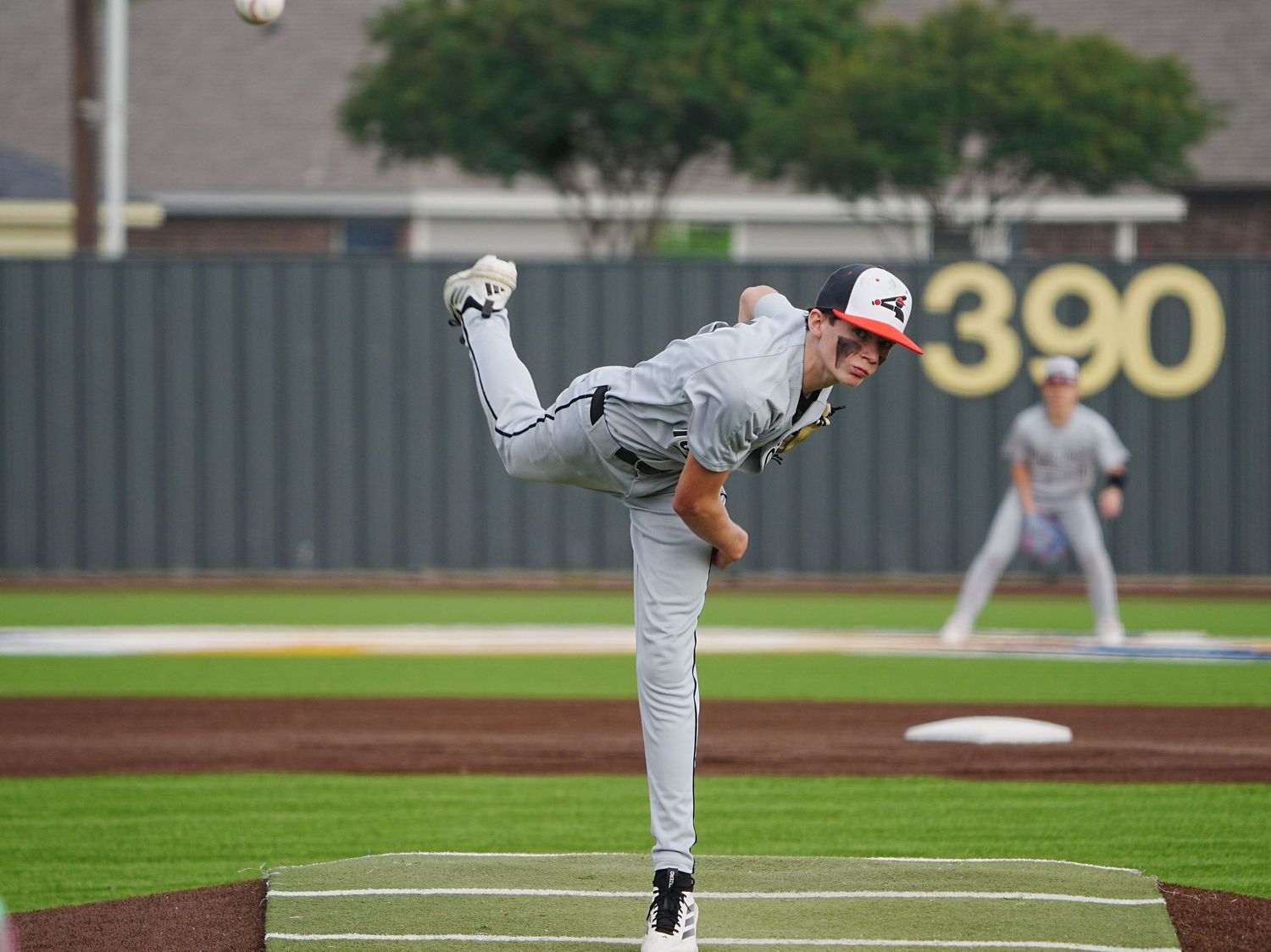 Baseball pitcher in gray uniform mid-throw on a professional mound, with a 390ft outfield wall visible in the background.