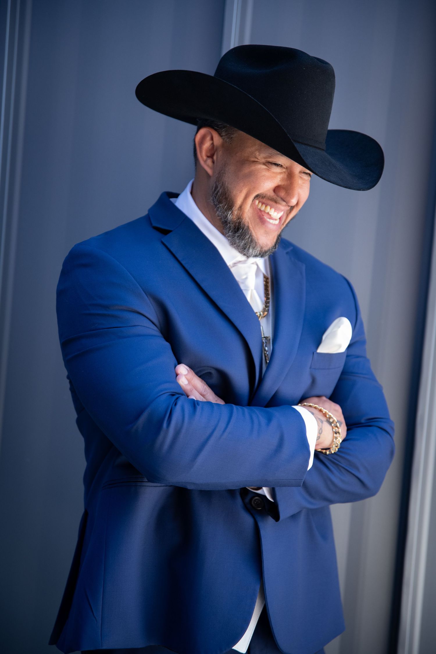 Person wearing blue suit and black cowboy hat smiling with arms crossed.