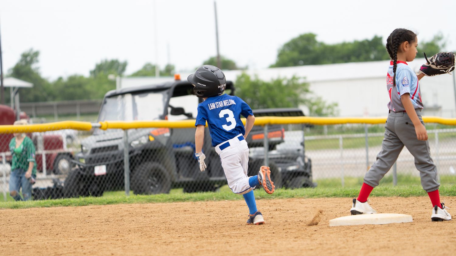Youth baseball game action as runner slides into base while defensive player reaches up to catch the ball.