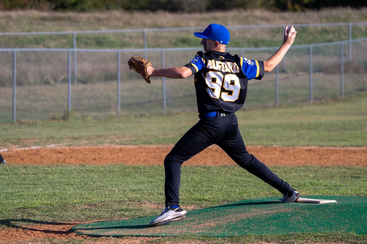 Baseball player in black uniform with number 35 and blue cap throws a pitch from the mound on a sunny day.