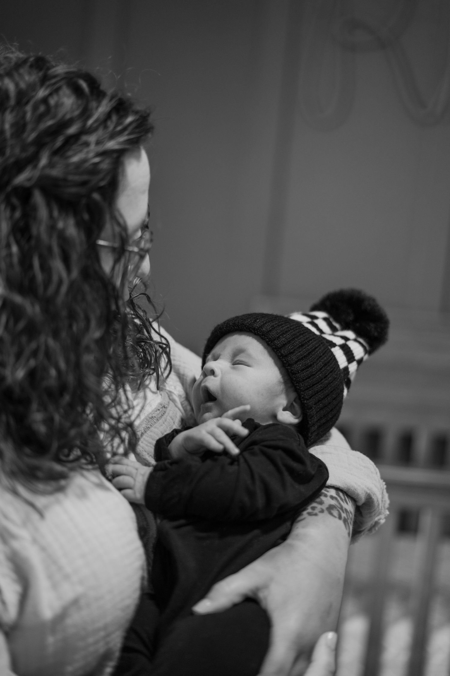 A tender black and white photograph shows a parent holding a sleeping baby wearing a knit winter hat with pom pom.