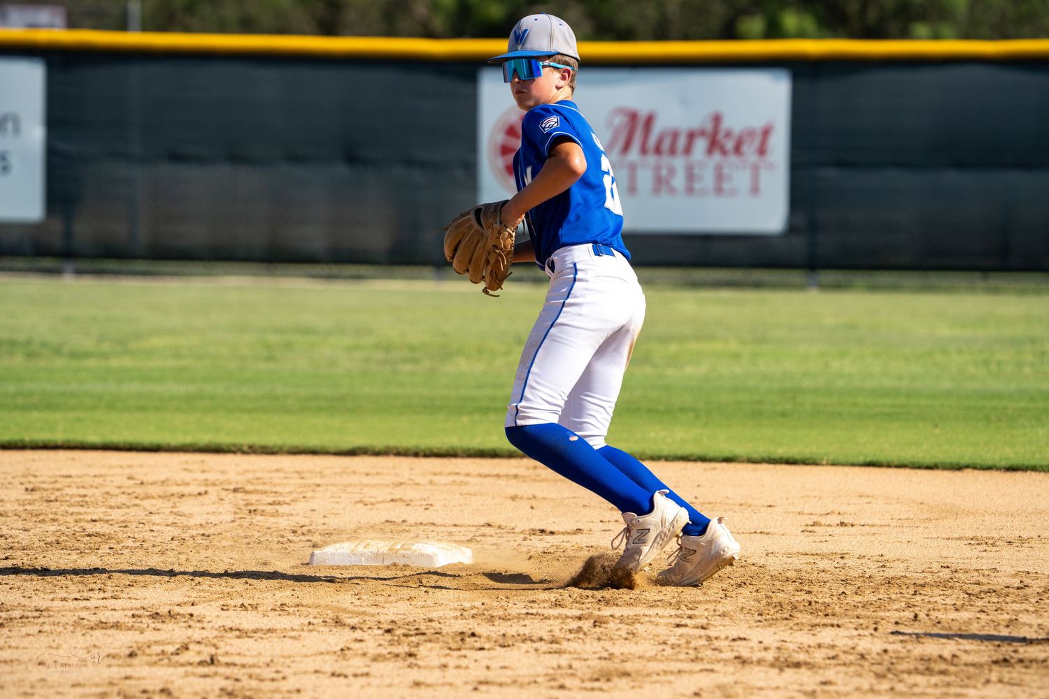 Softball player in blue uniform and white pants throws from the infield on a sunny day at the ballpark.