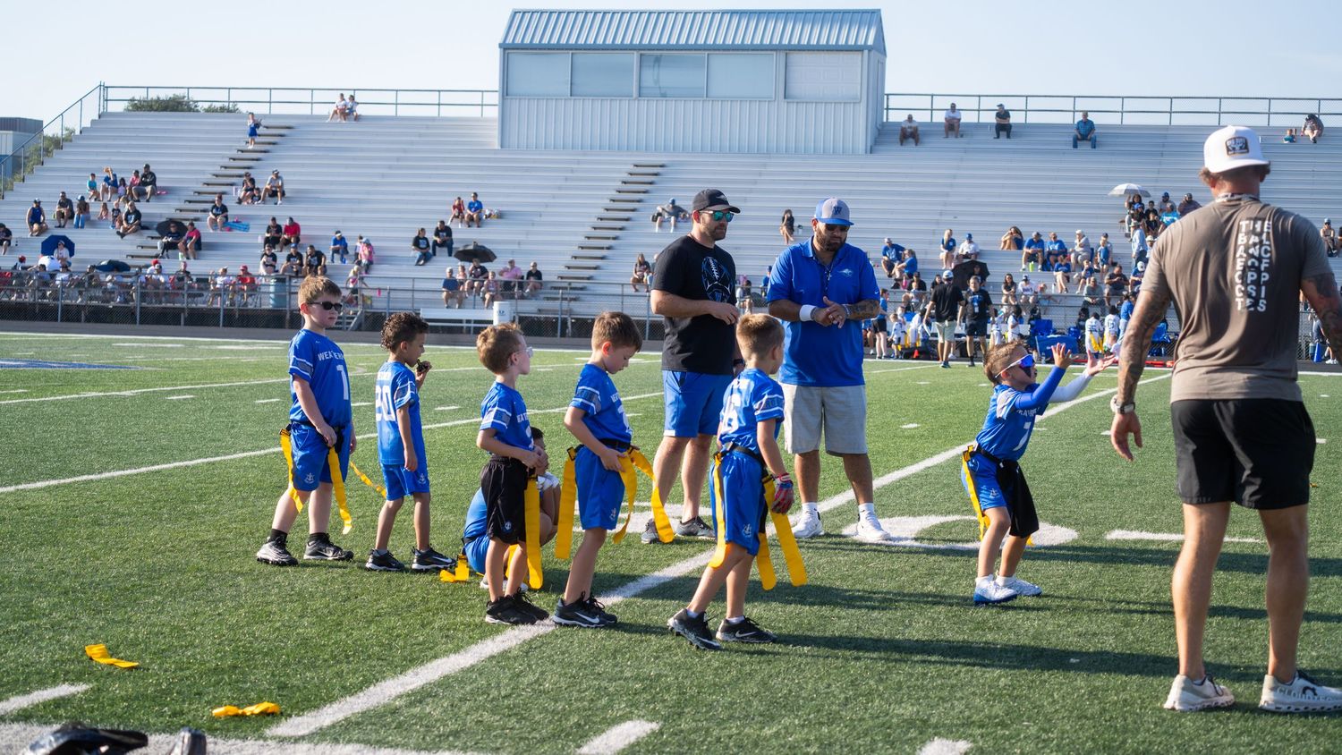 Football players practicing drills on a turf field as coaches oversee their training session.