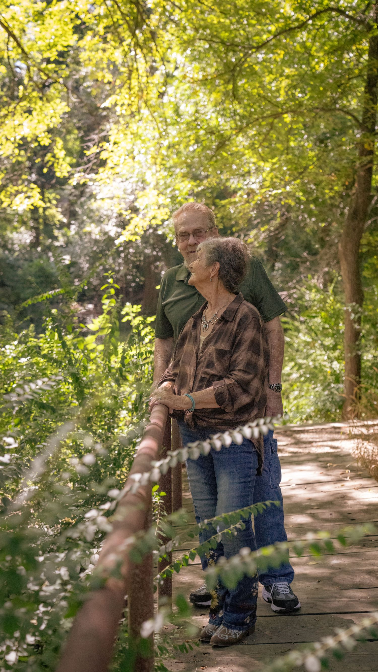 A couple enjoying a peaceful moment together on a wooden walkway through lush forest.