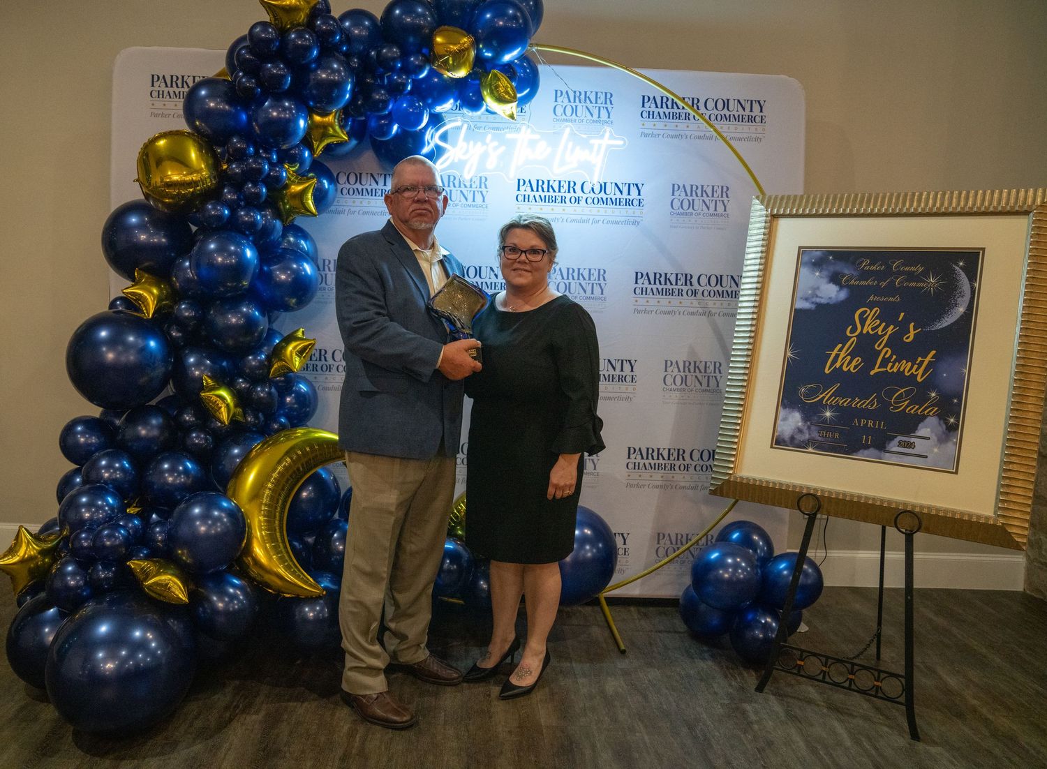 A couple poses for a photo at an awards ceremony with elegant balloon decor.