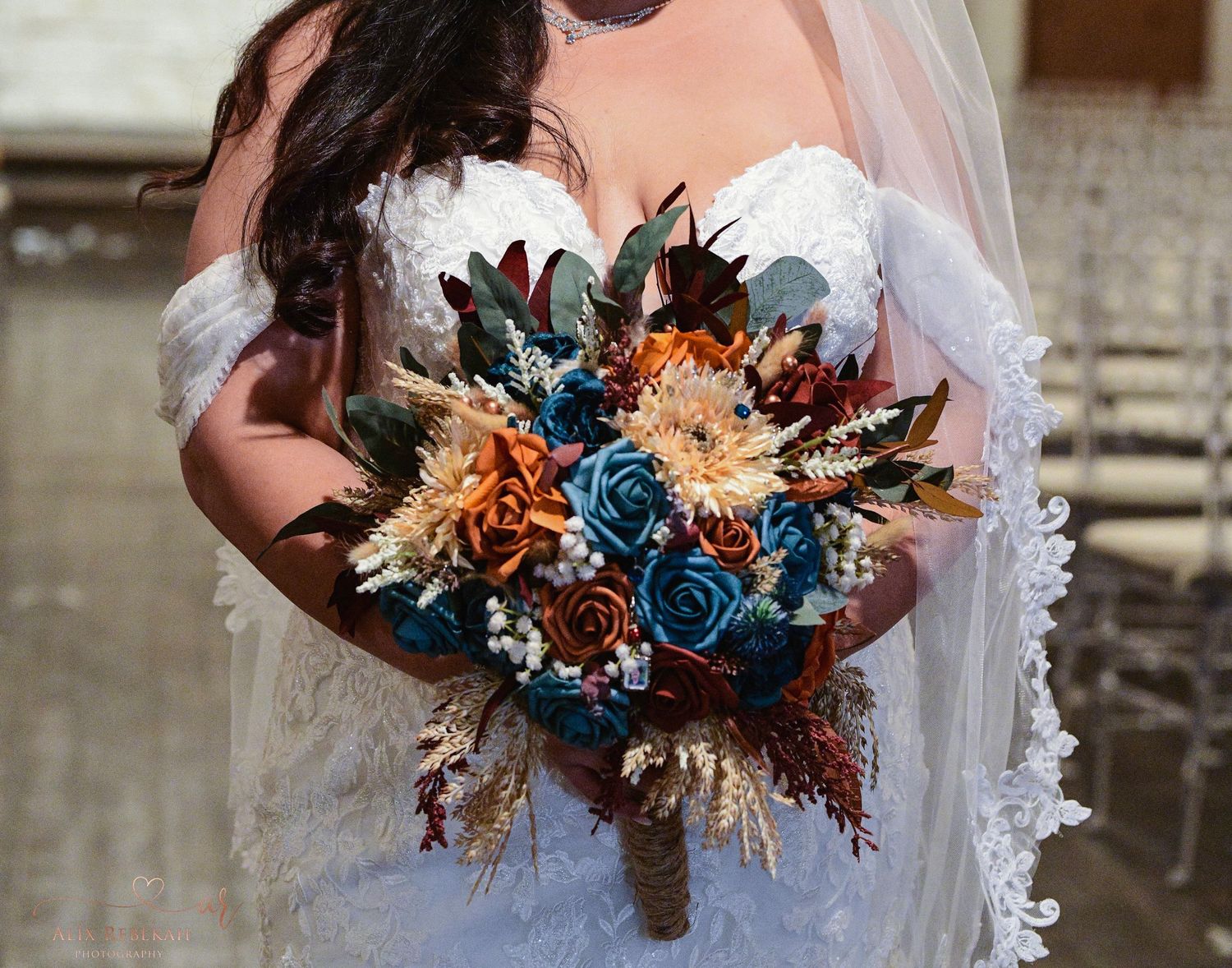 A wedding bouquet featuring blue roses, orange flowers, and dark foliage against a white lace dress.