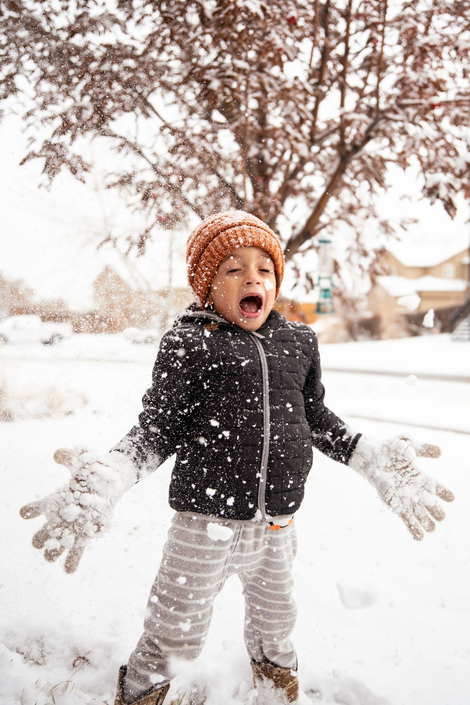 Joyful child playing in falling snow wearing winter clothing and knit hat.