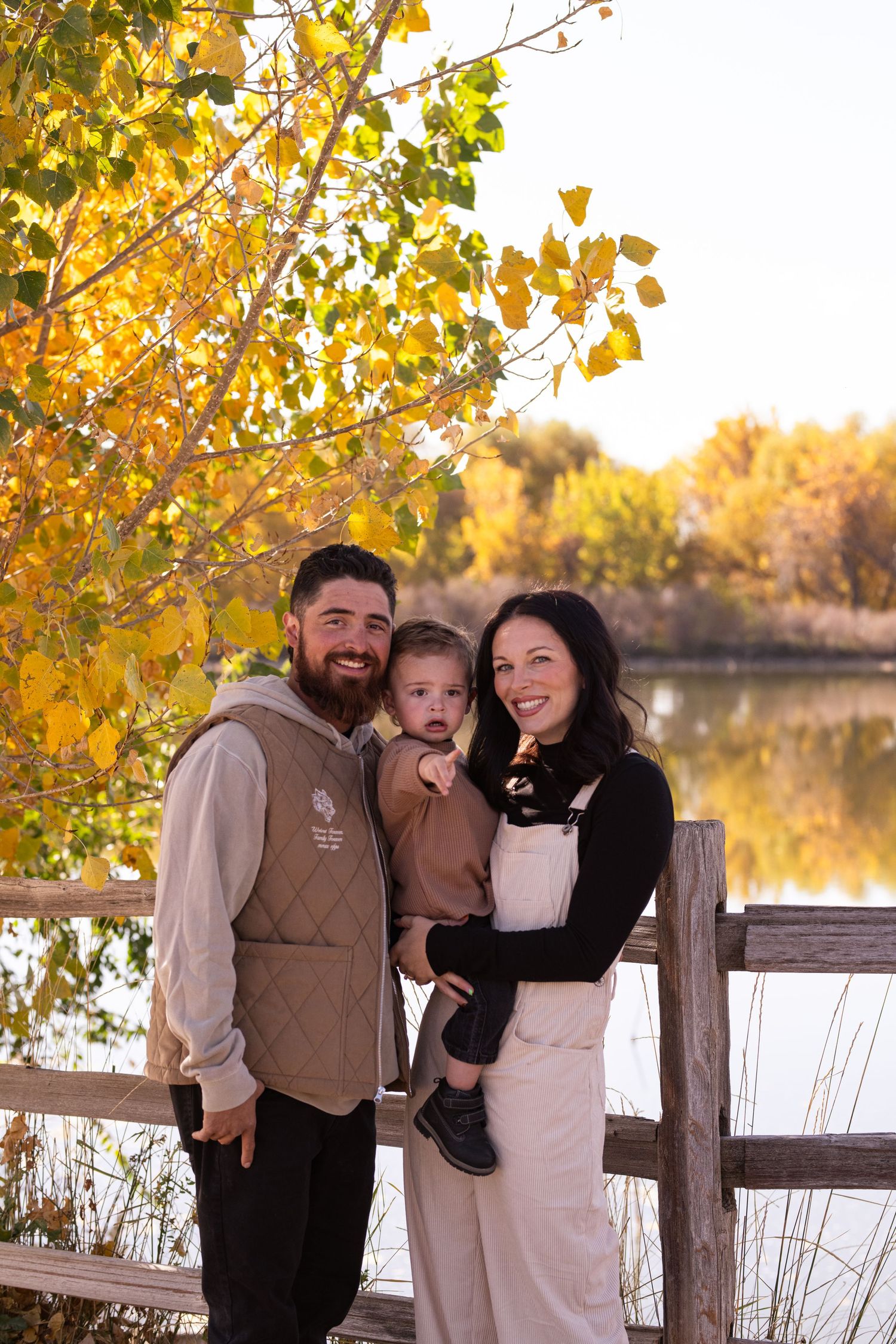 Casual family portrait by lake with golden autumn leaves in background.